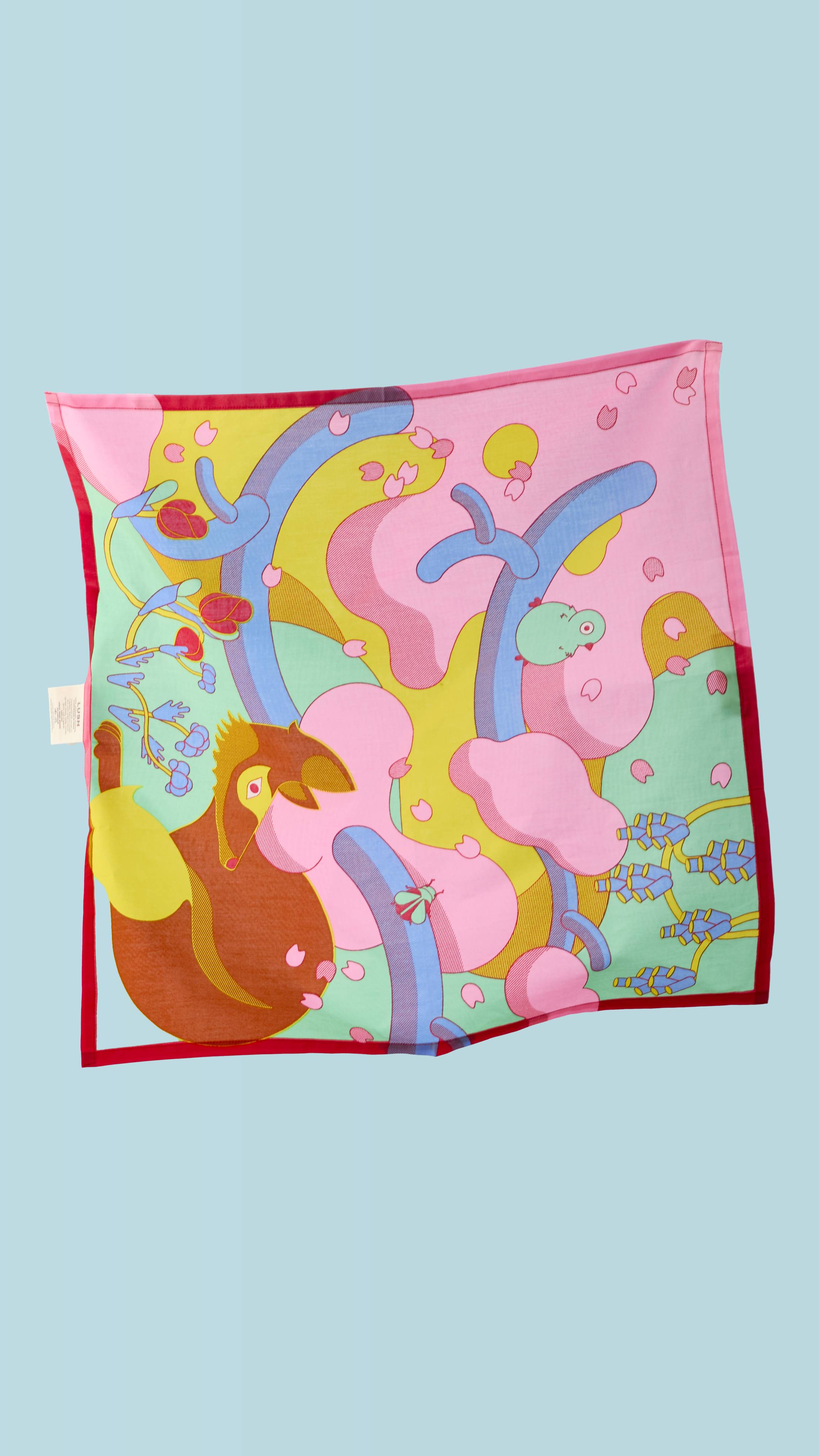 The "Forest Awakens" knot wrap is suspended in the air on a blue background. It has a colourful illustration with a stylised brown fox, a turquoise bird, and pink cherry blossom petals. The background is a mix of bright swirls with red tulip accents.