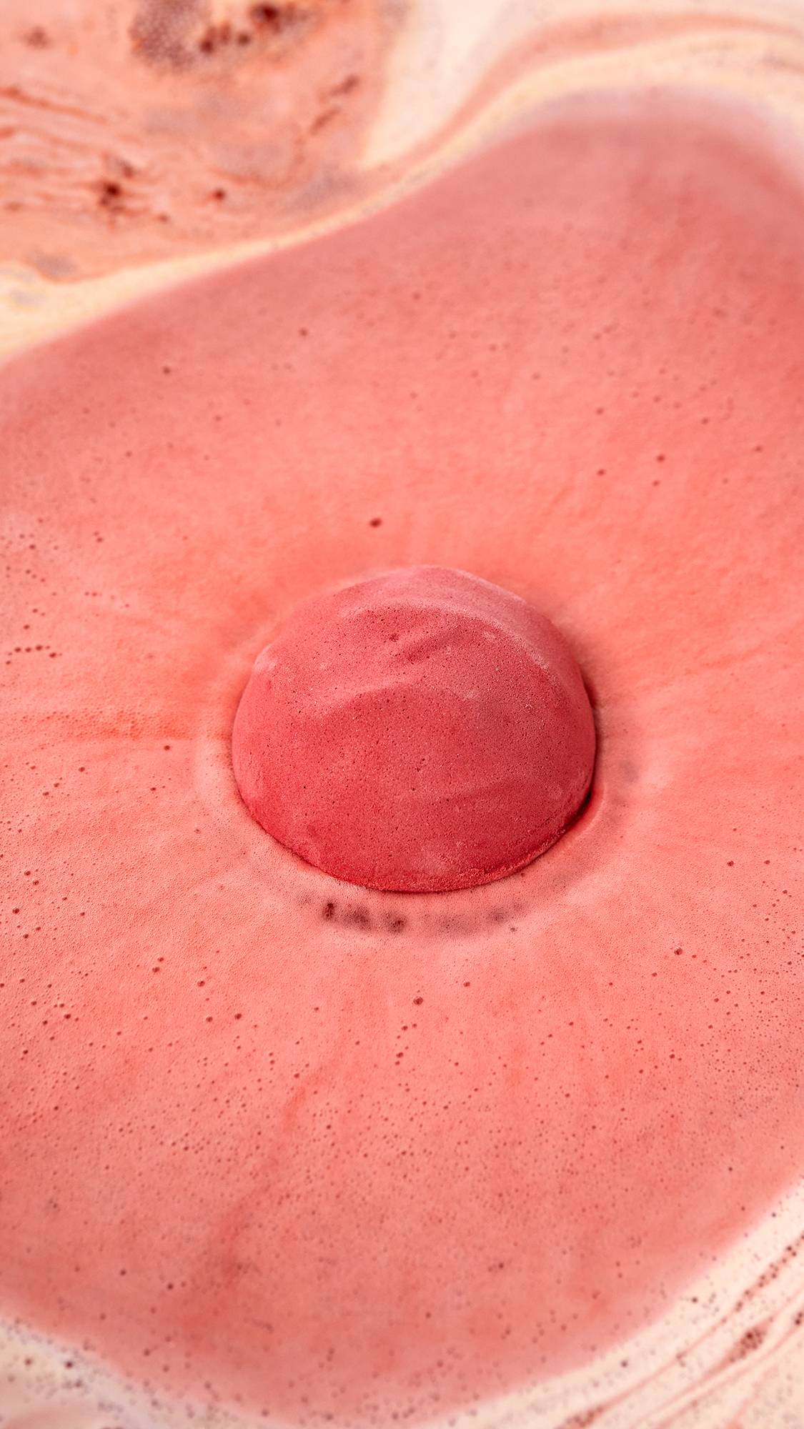 The image shows an aerial view of the Sticky Dates bath bomb as it starts to dissolve in the bath. The product is creating a thick blanket of warm, rich, rust-coloured, velvety foam. 