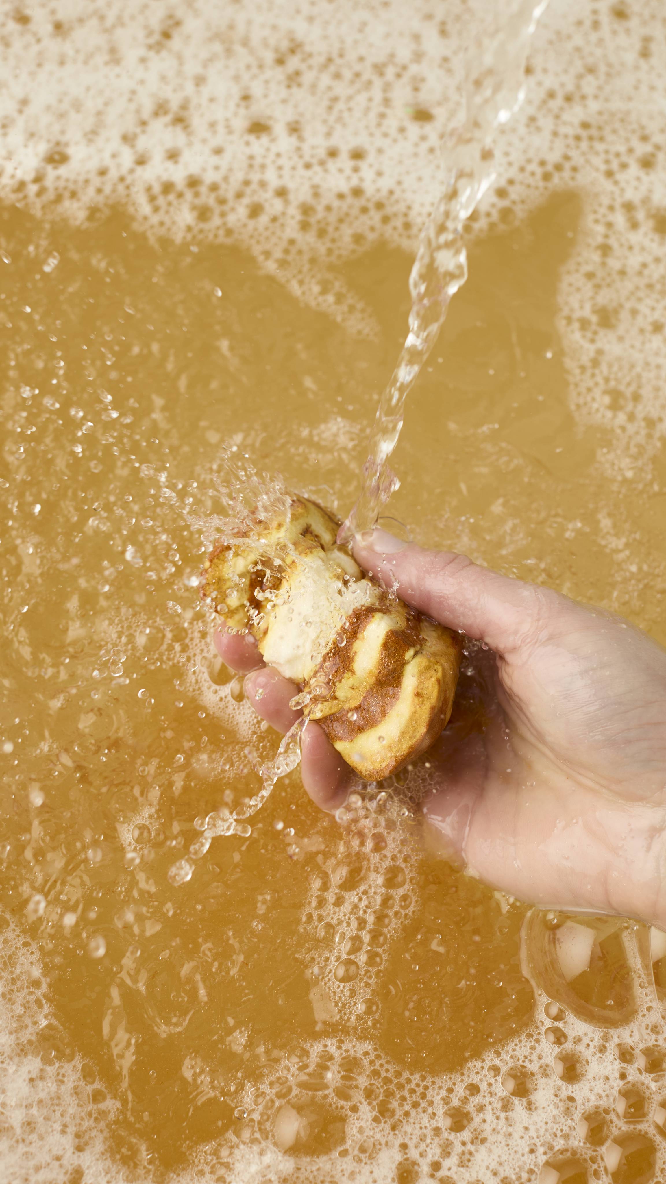 A circular Swirly Sticky Dates bubble bar featuring a marbled spiral design of rich cocoa brown and sandy beige. It has a rustic, crumbly texture and is presented against a neutral grey background.