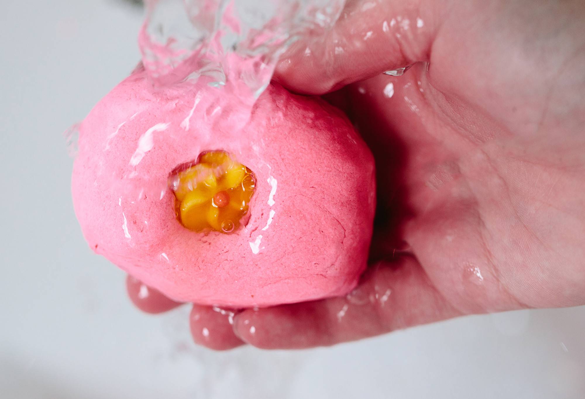 Creamy Candy, a small, rectangular, pink bubble bar with a candy flower in its centre, is held under running water.