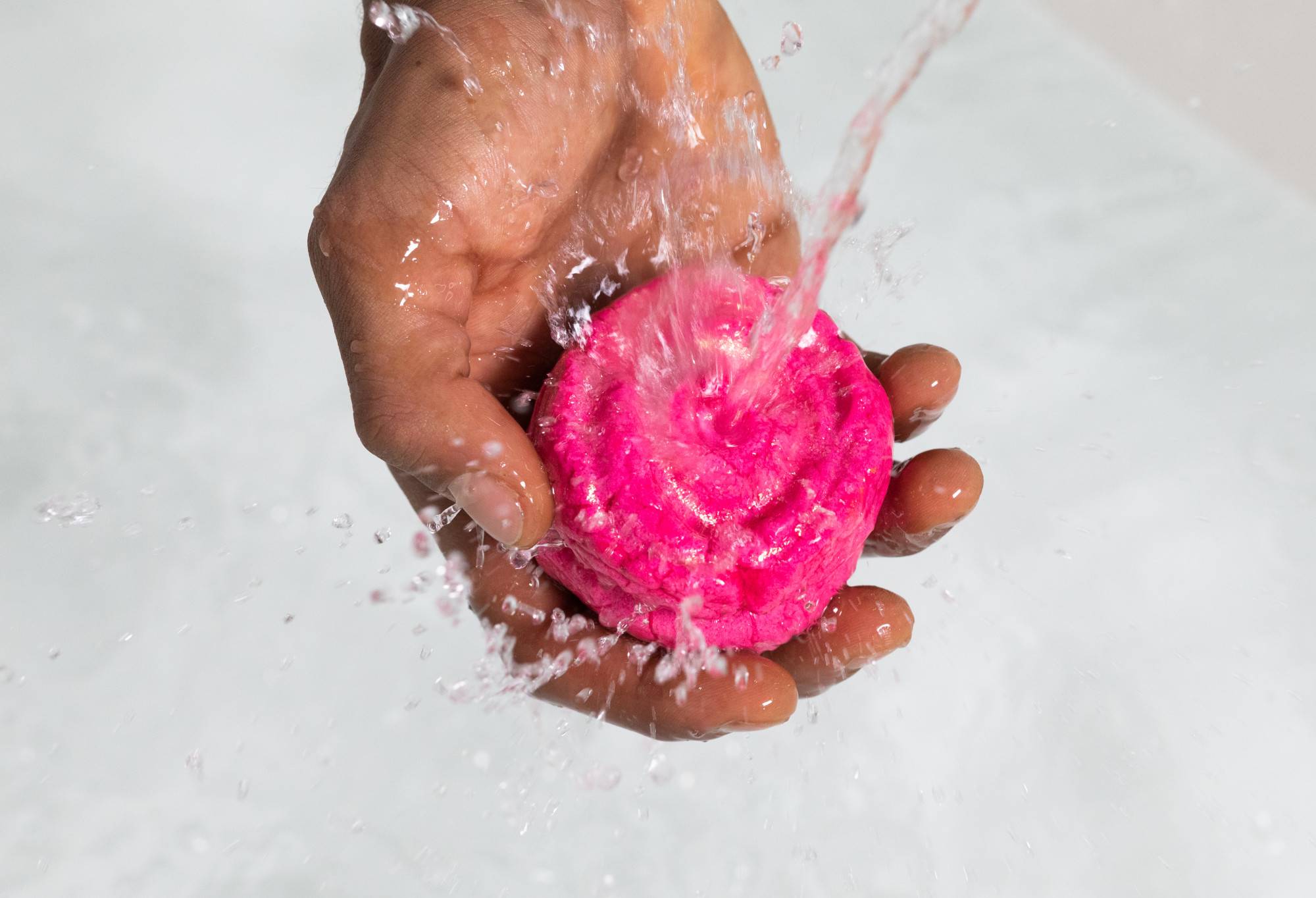 A hand holds Rose Jam under running water as the water bounces off. The background is clear water.