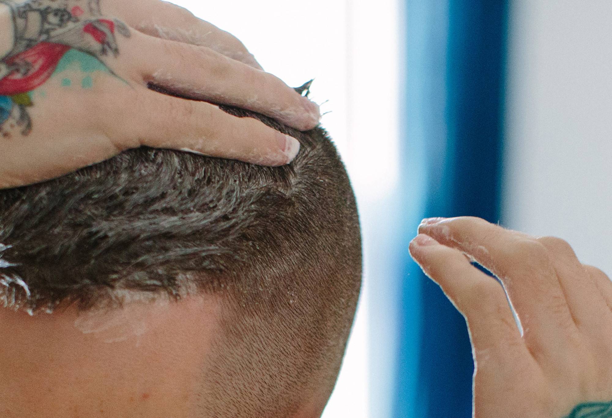 A person with short hair, shaved sides and tatoos rubs Roots, a creamy hair treatment, through the top section of their hair.