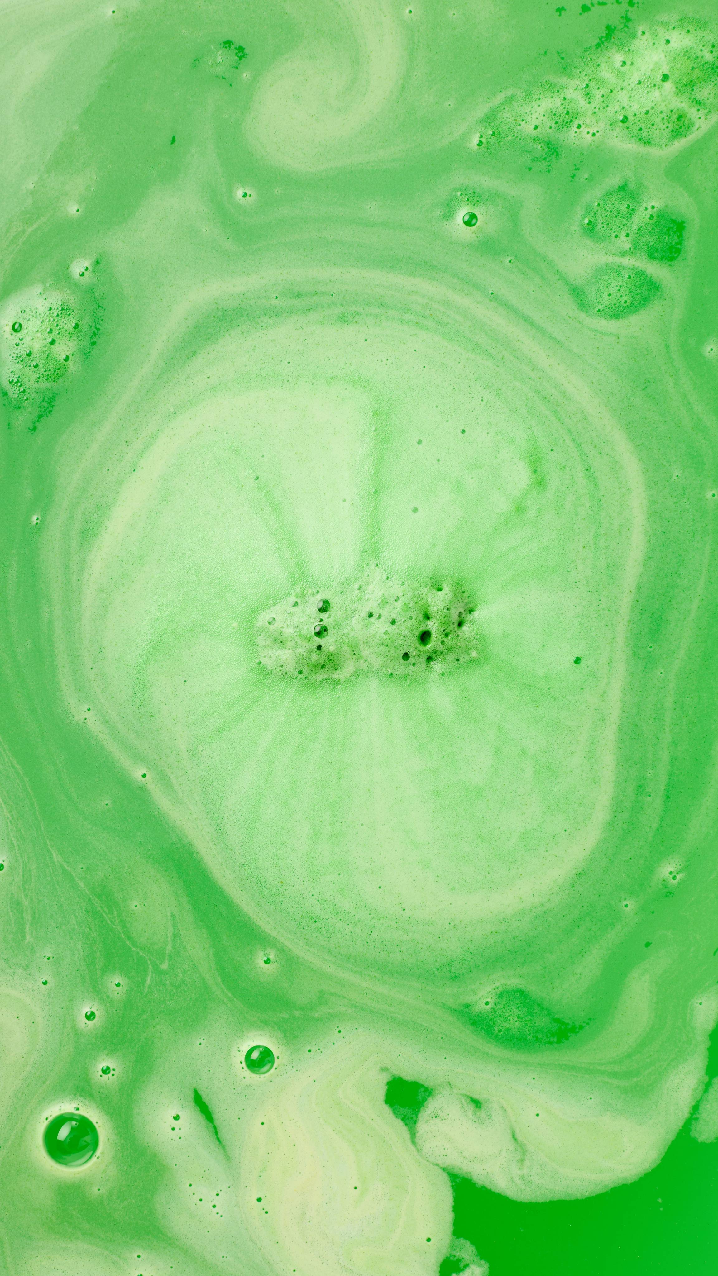 The image shows swirling bath art from the Father Christmas bath bomb, a vibrant lime green. Abundant green foam and bubbles cover the water, with a central cluster of active bubbles marking the fizzing core.