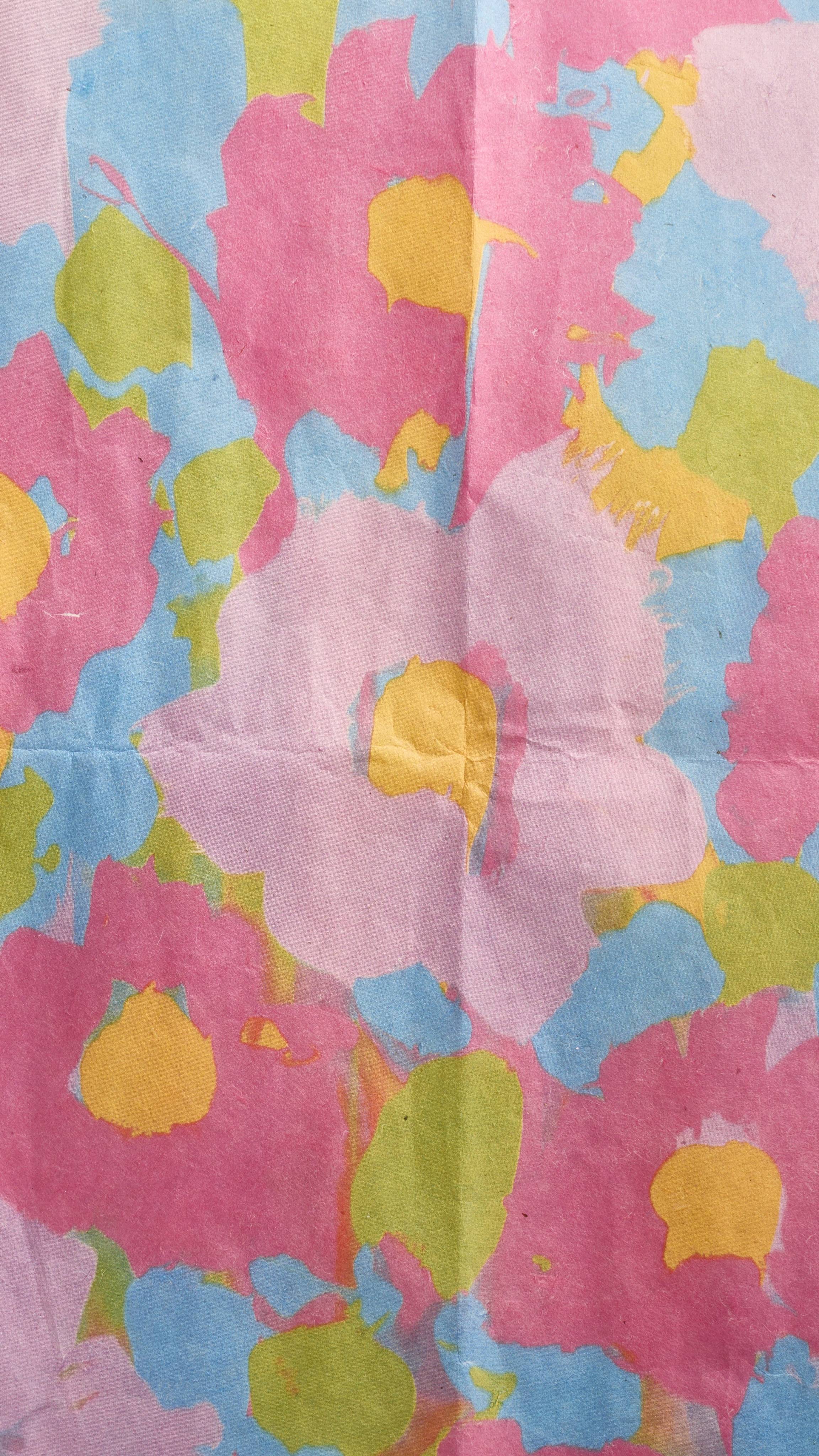 A vibrant close-up shows a sheet of the "Flower Up" Lokta paper, featuring a hand-painted floral design with light and dark pink flowers with yellow centres, and large, lush green leaves.