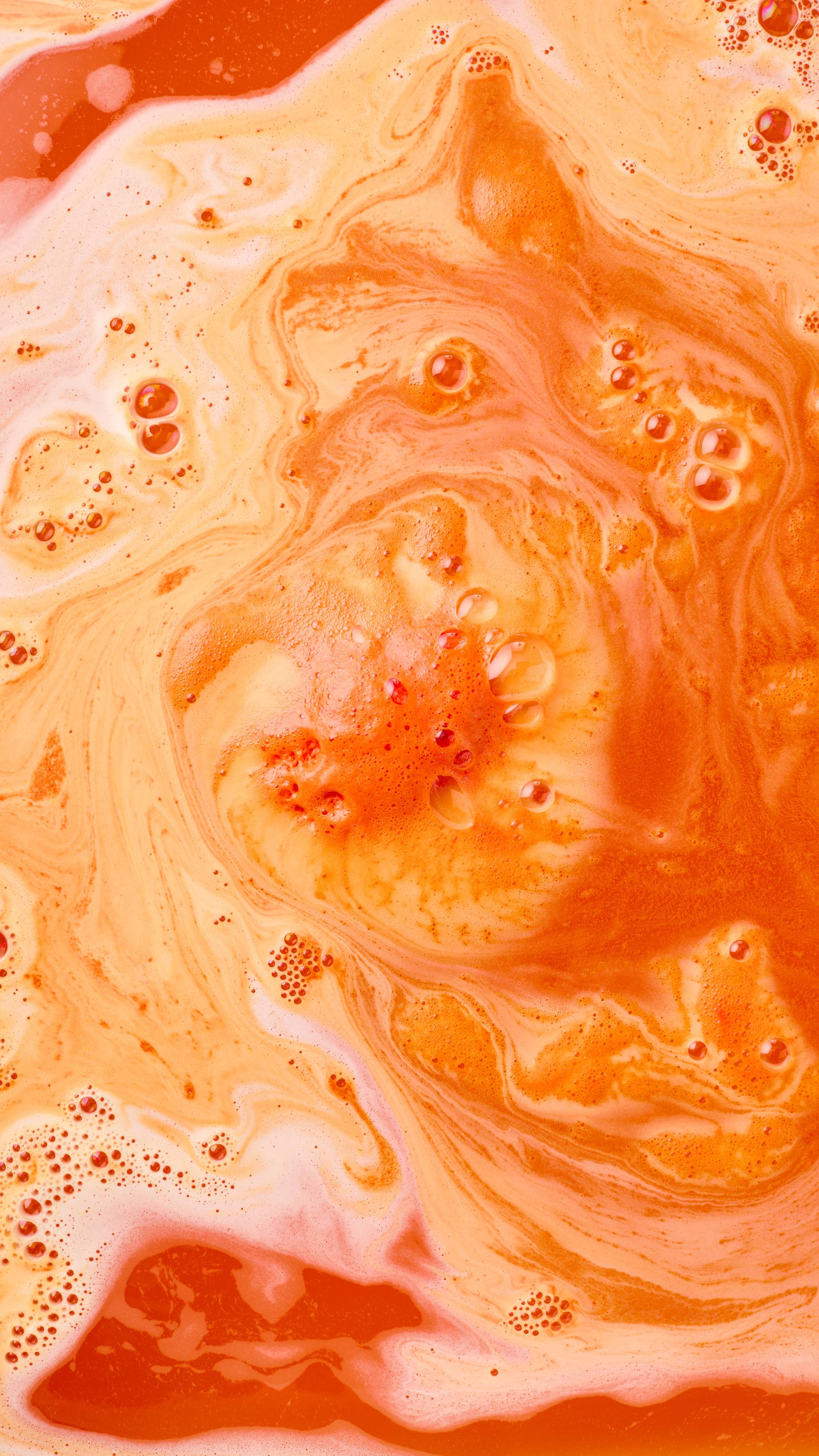 The image shows vibrant orange bath water largely covered in abundant white, orange and yellow, frothy bubbles generated by the 'Ginger Tom' bath bomb.