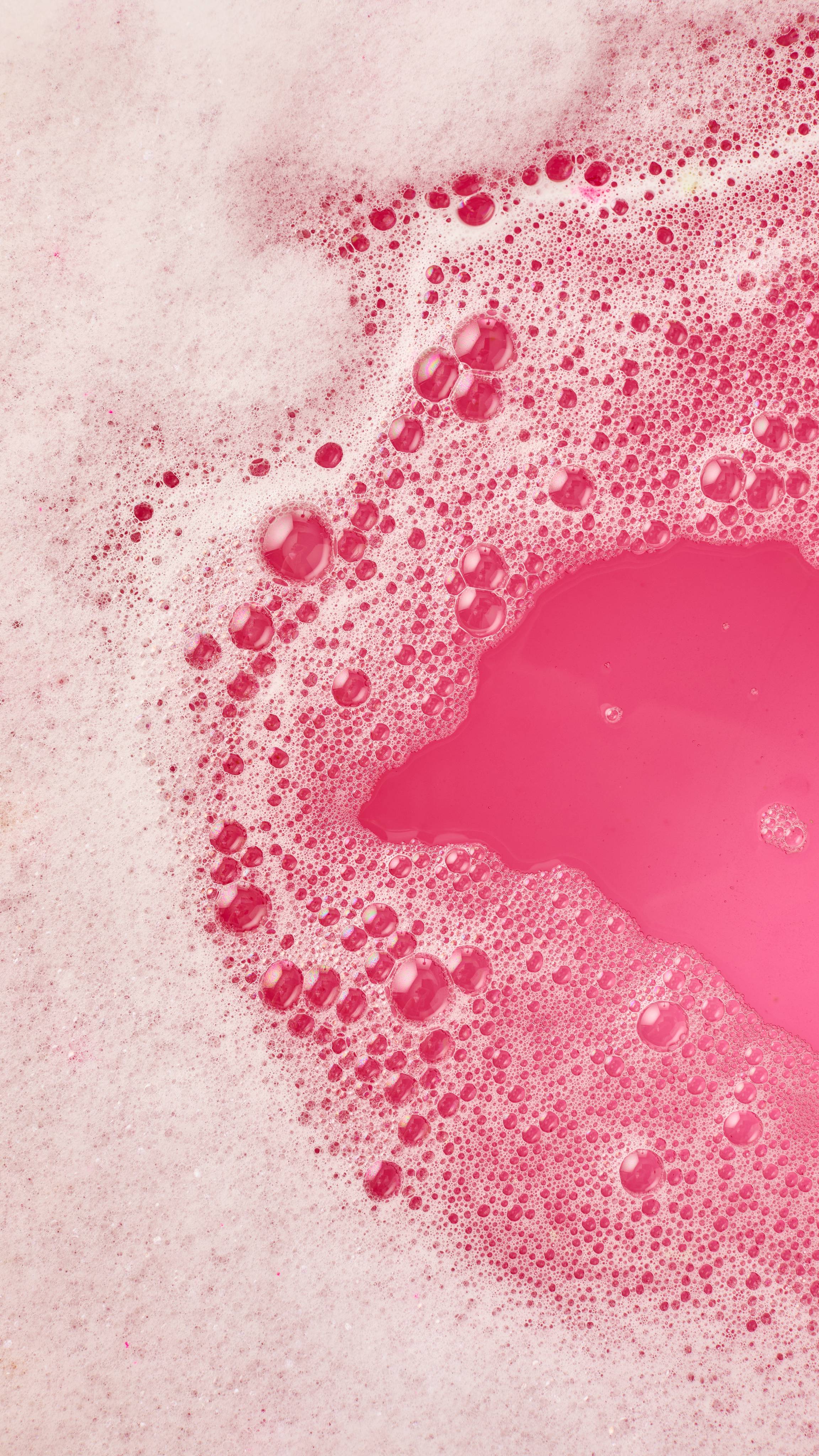 The image shows vibrant pink bath water covered in abundant white, frothy bubbles. Darker pink channels of water wind through the foam, creating an abstract landscape from the 'Invaders from Mars' bubble bar.
