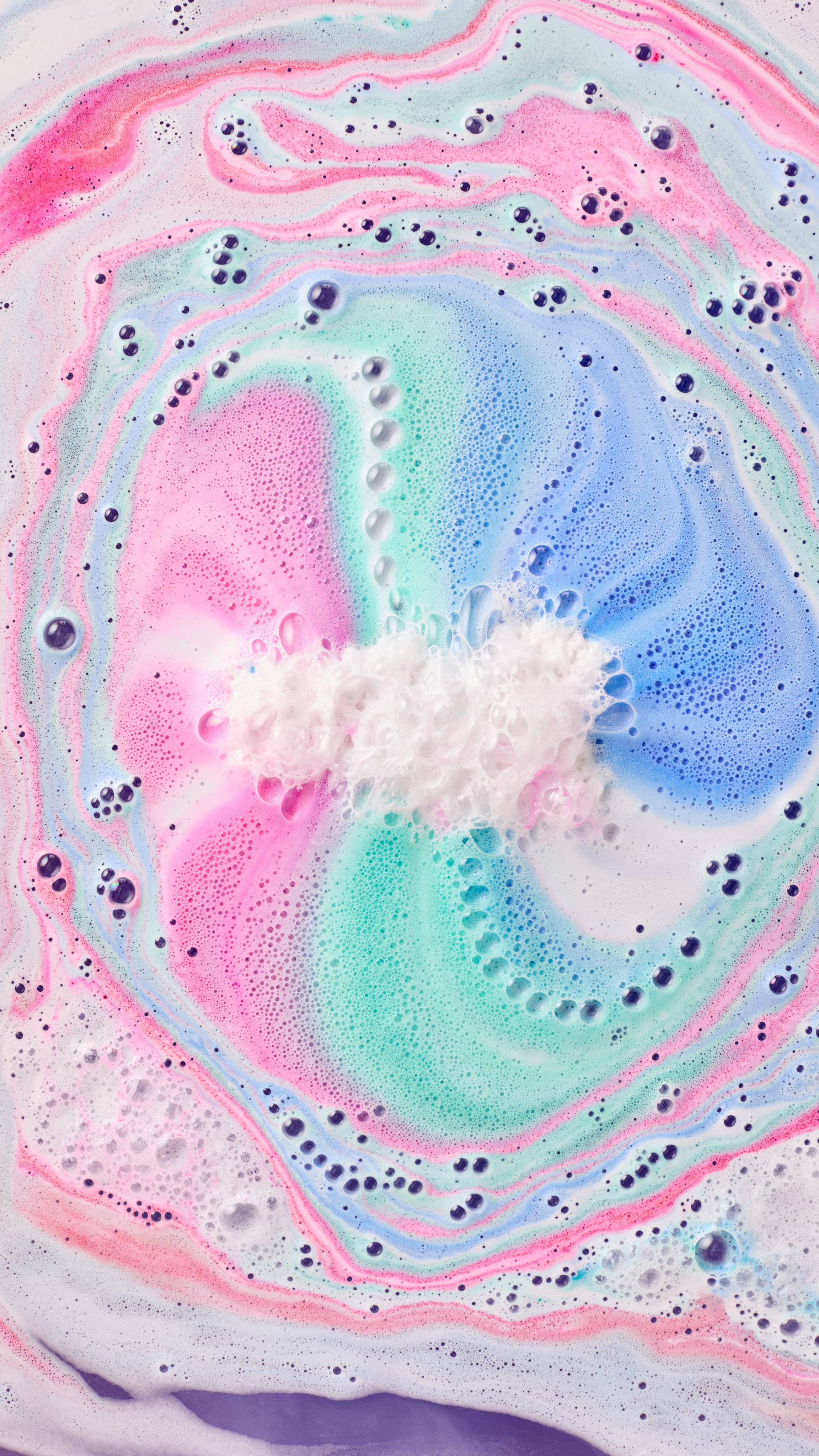 The image shows swirling bath art from the Mad Scientist Bath Bomb, a vibrant blend of hot pink, bright blue, and turquoise hues. Large, foamy swirls radiate from a white central area, mixing with purple at the bottom.