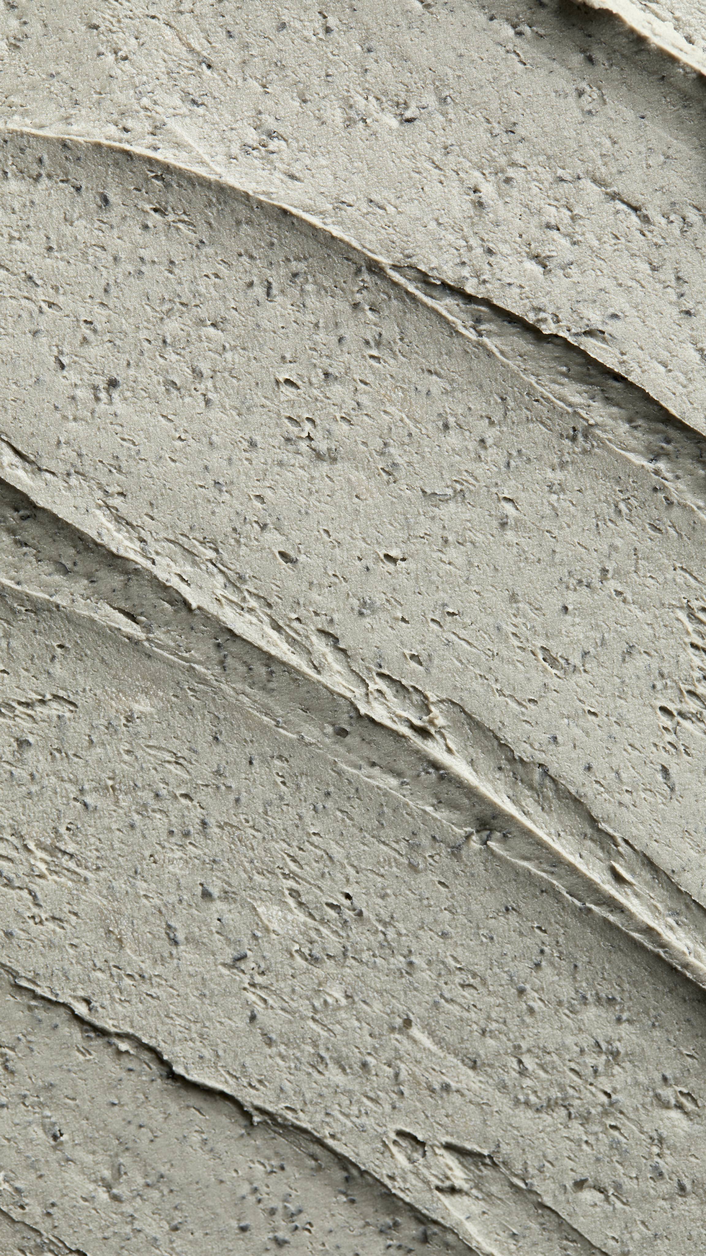 A textured, close-up macro shot of thick diagonal smears of greyish-green Lush Persephone's Pomegranate face mask. The rough paste features distinct ridges from application, filled with numerous tiny exfoliating specks.