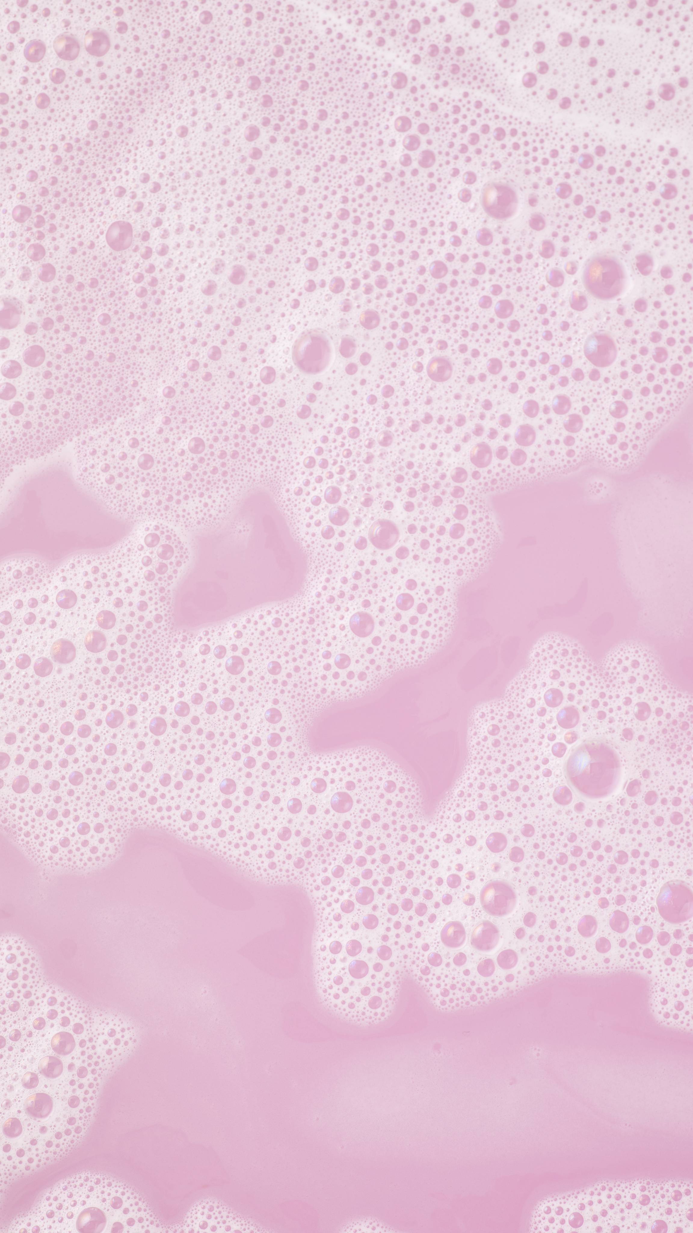 A close-up of pale pink, foamy bath water with white bubbles on the surface, created by the Raspberry mini bath wand.