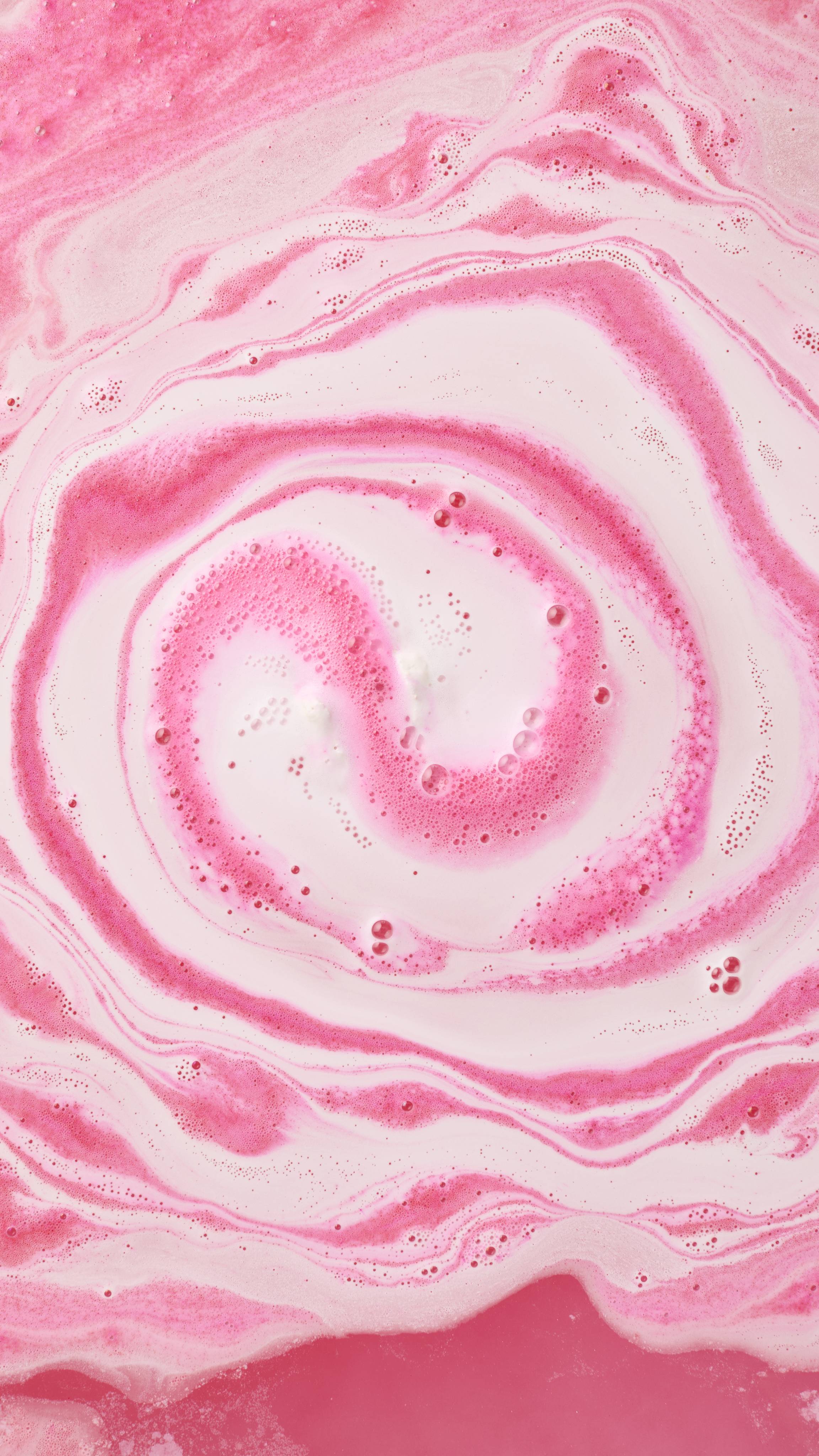 An aerial image of the bath art created by the Sweetheart bath bomb. A swirling ripple of pink and white swirls radiates across the foamy surface of the bath.