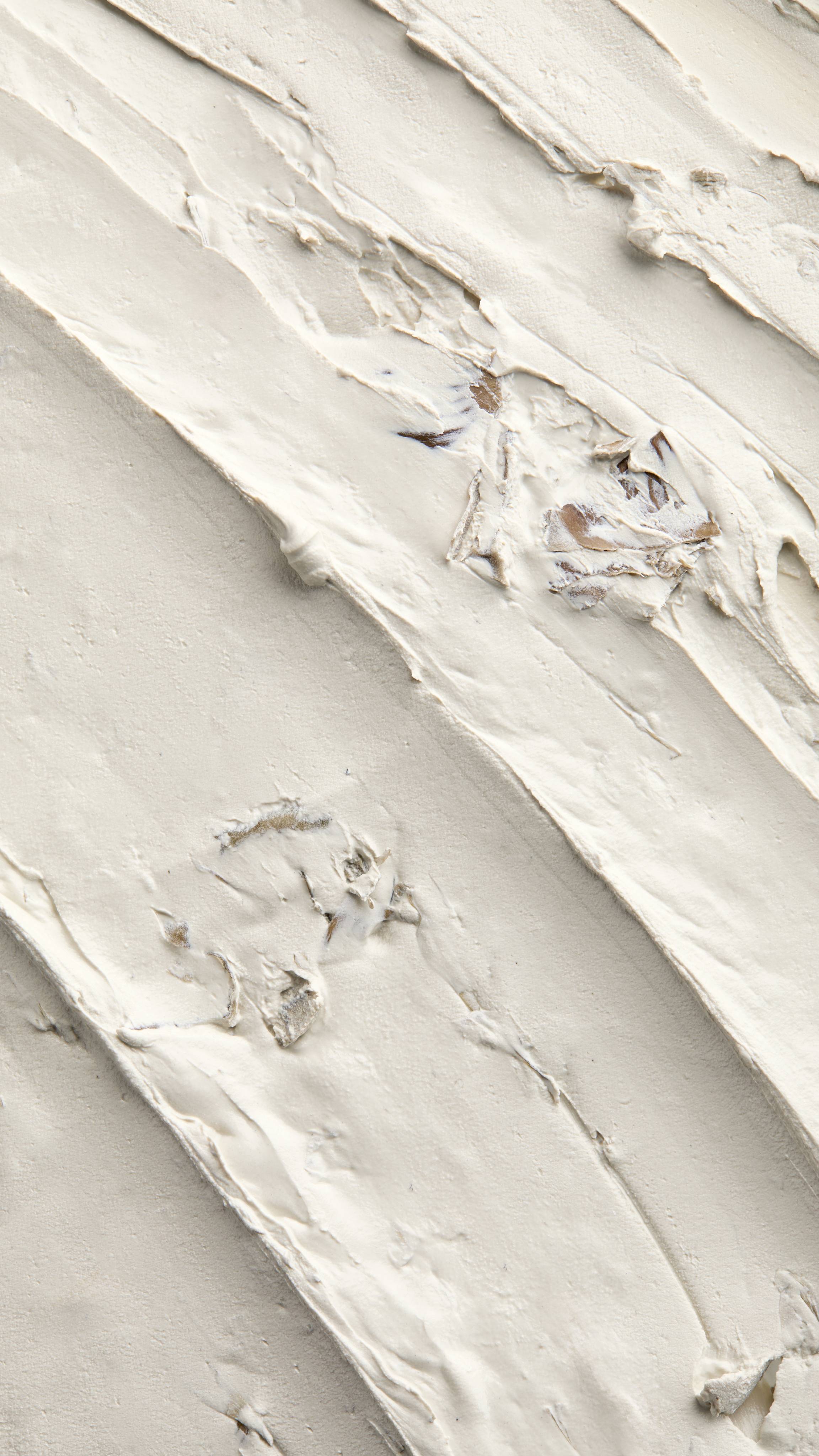 A textured, close-up macro shot of thick diagonal smears of Lush Who Runs The World? Ghouls! face mask. The smooth, light-coloured paste features visible ridges from application and small chunks of embedded brown natural ingredients.