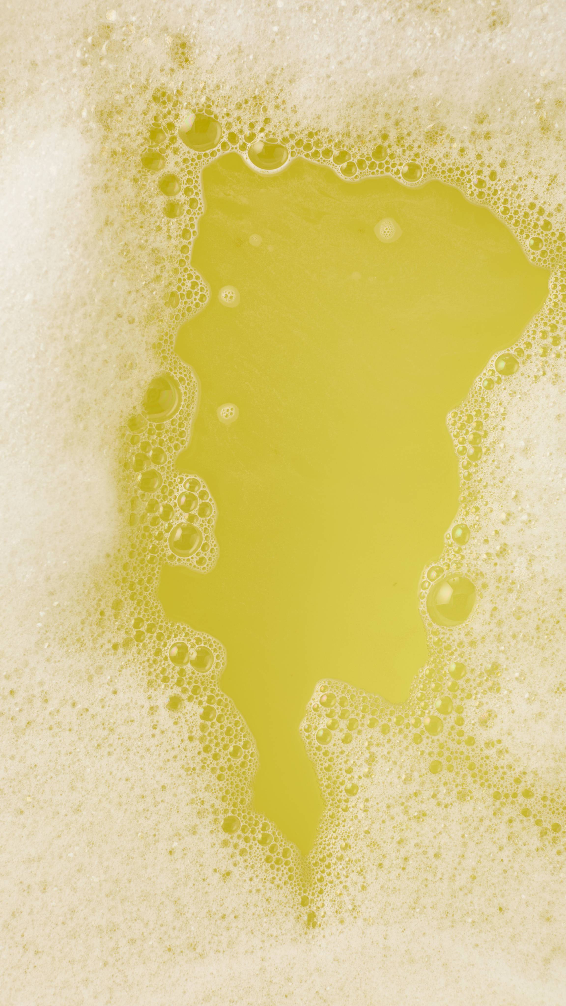A close-up, aerial view of a thick layer of pale yellow bubbles and foam covering the surface of the bathwater, created by the Bananas For You bubbleroon bubble bar. The bubbles vary in size, creating a dense, frothy texture with soft yellow hues.