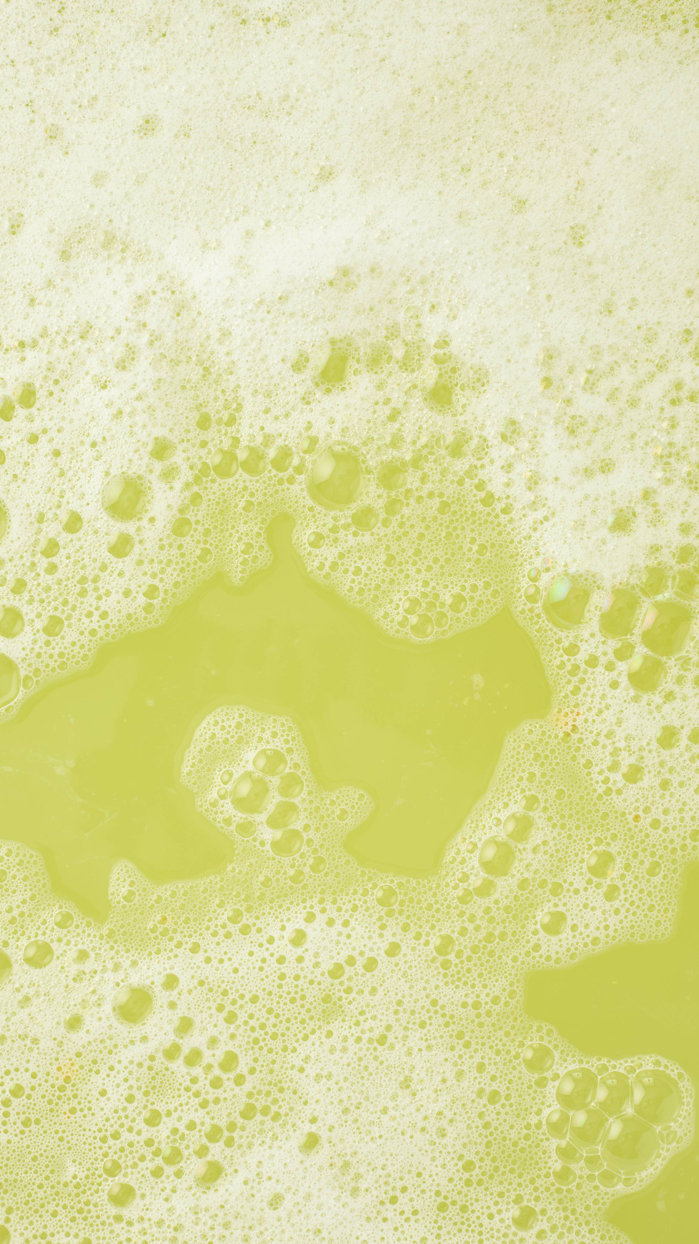 An aerial view image of the bathwater after using the "Easy Peasy Lemon Squeezy" bubble bar. The water has turned a pale yellow colour with a blanket of thick foamy bubbles on top.