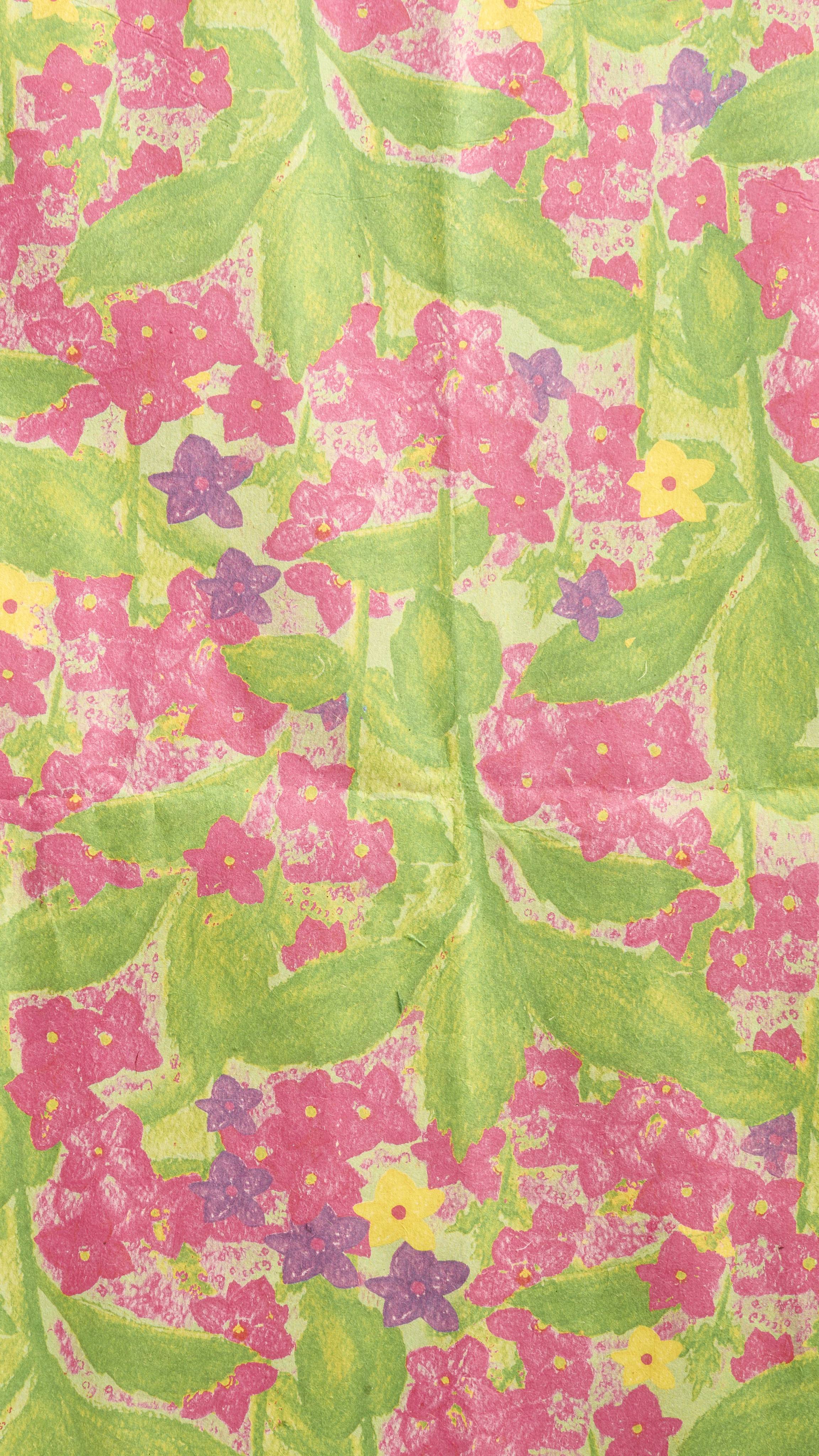 A vibrant close-up shows a sheet. of the "Garden in Spring Lokta paper, featuring a hand-painted floral design with pink, purple, yellow, and blue flowers, and large, lush green leaves.