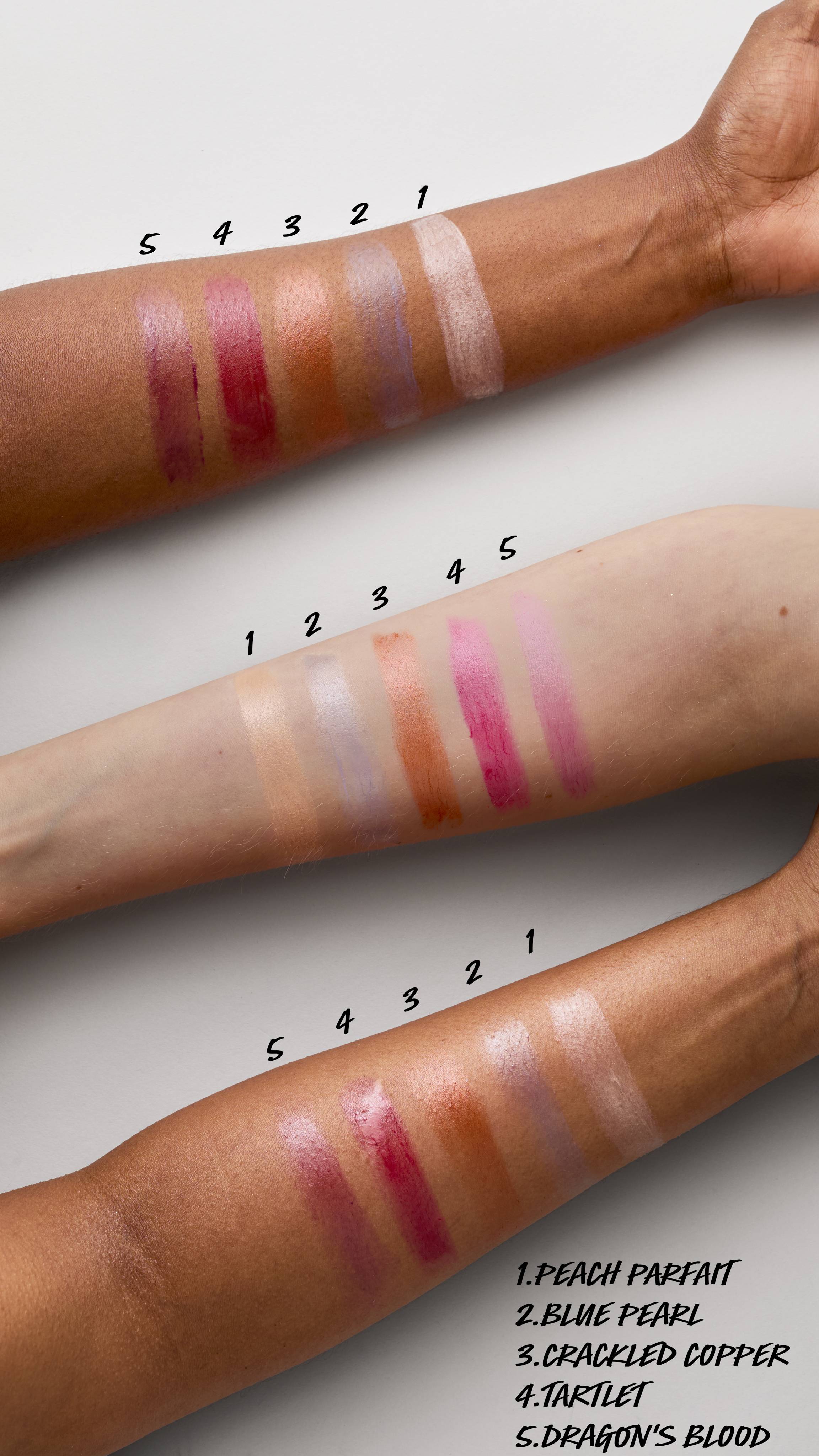 The image shows an aerial view of three forearms of differing skin tones. Across each of the arms are swatched the five Firework Lush lip creams, from light to dark, to display how they show on different skin tones. 