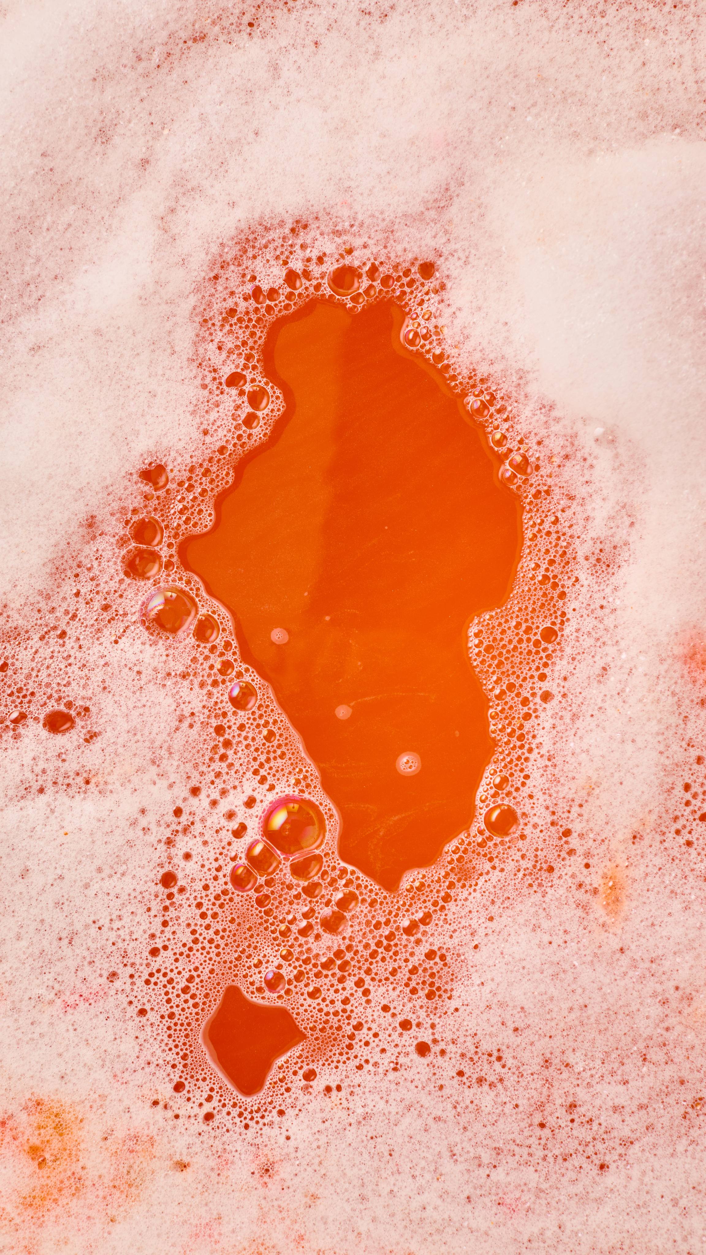 The image shows vibrant orange bath water just visible beneath abundant white, frothy bubbles from the 'Pumpkin Spice' bubble bar.