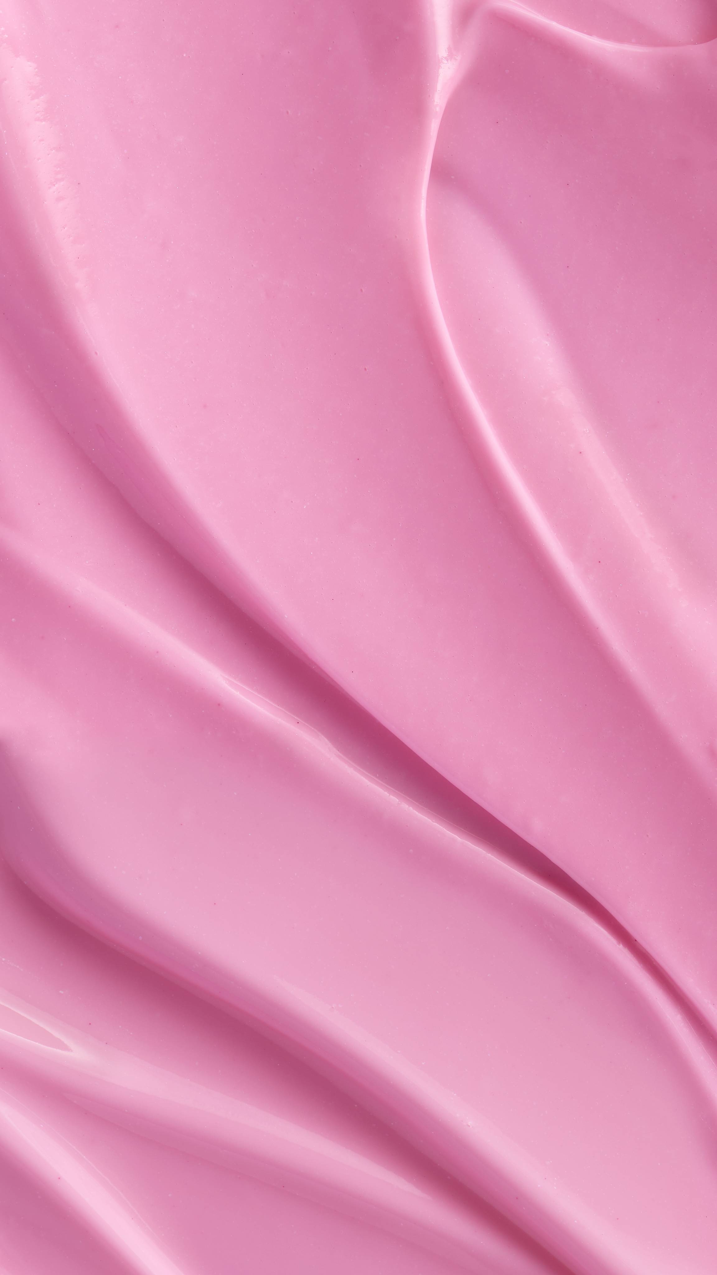 A close-up of a rich, pink, creamy product swirled into soft, textured peaks and valleys. The smooth, glossy surface and vibrant colour suggest the delightful texture of LUSH Snow Fairy body lotion.