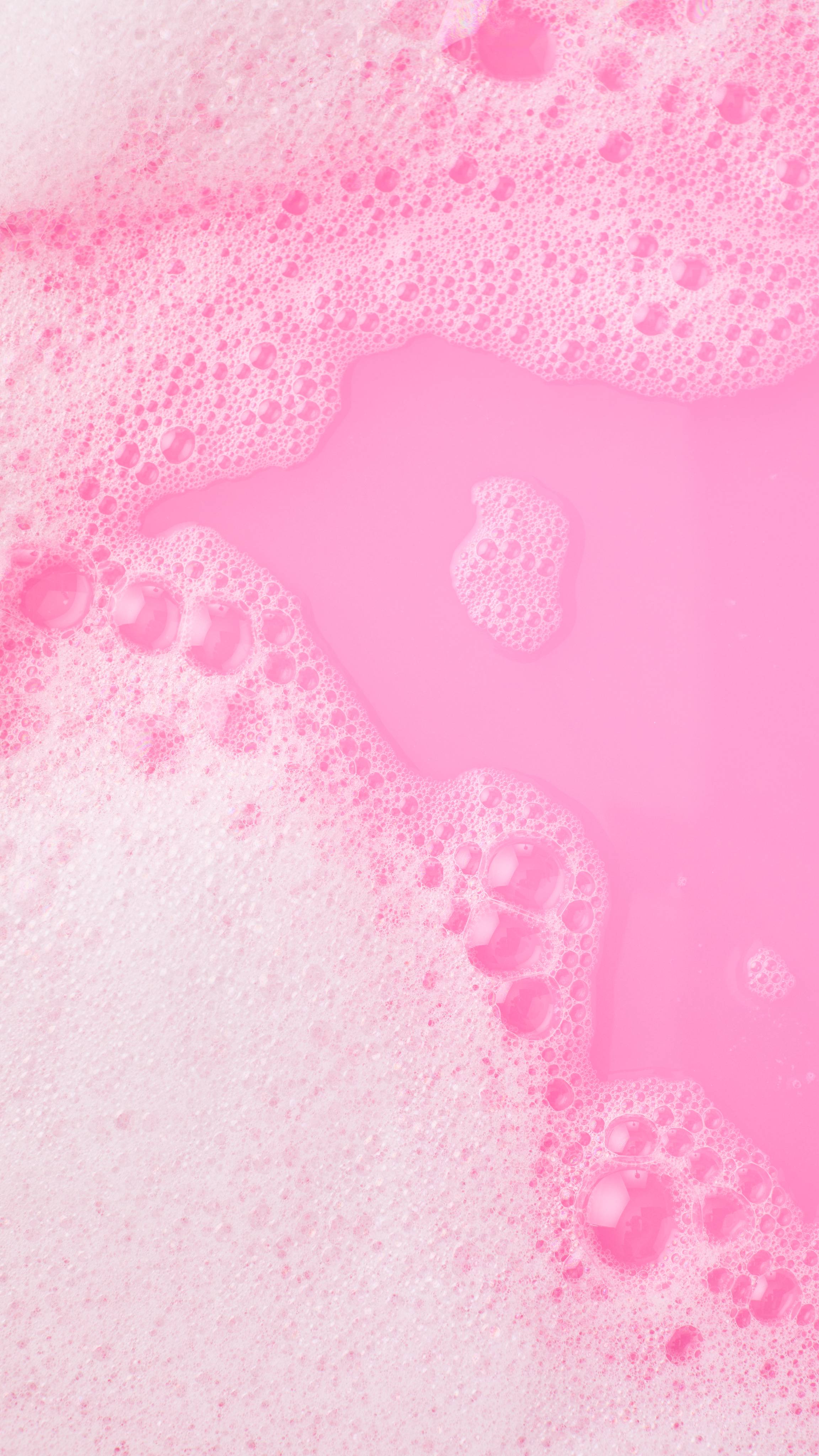 A close-up, aerial image of the bath water after using the Lush, Snow Fairy Wand bubble bar. There is a blanket of thick, fat bubbles with bright, bubblegum-pink bath water visible through a large gap. 