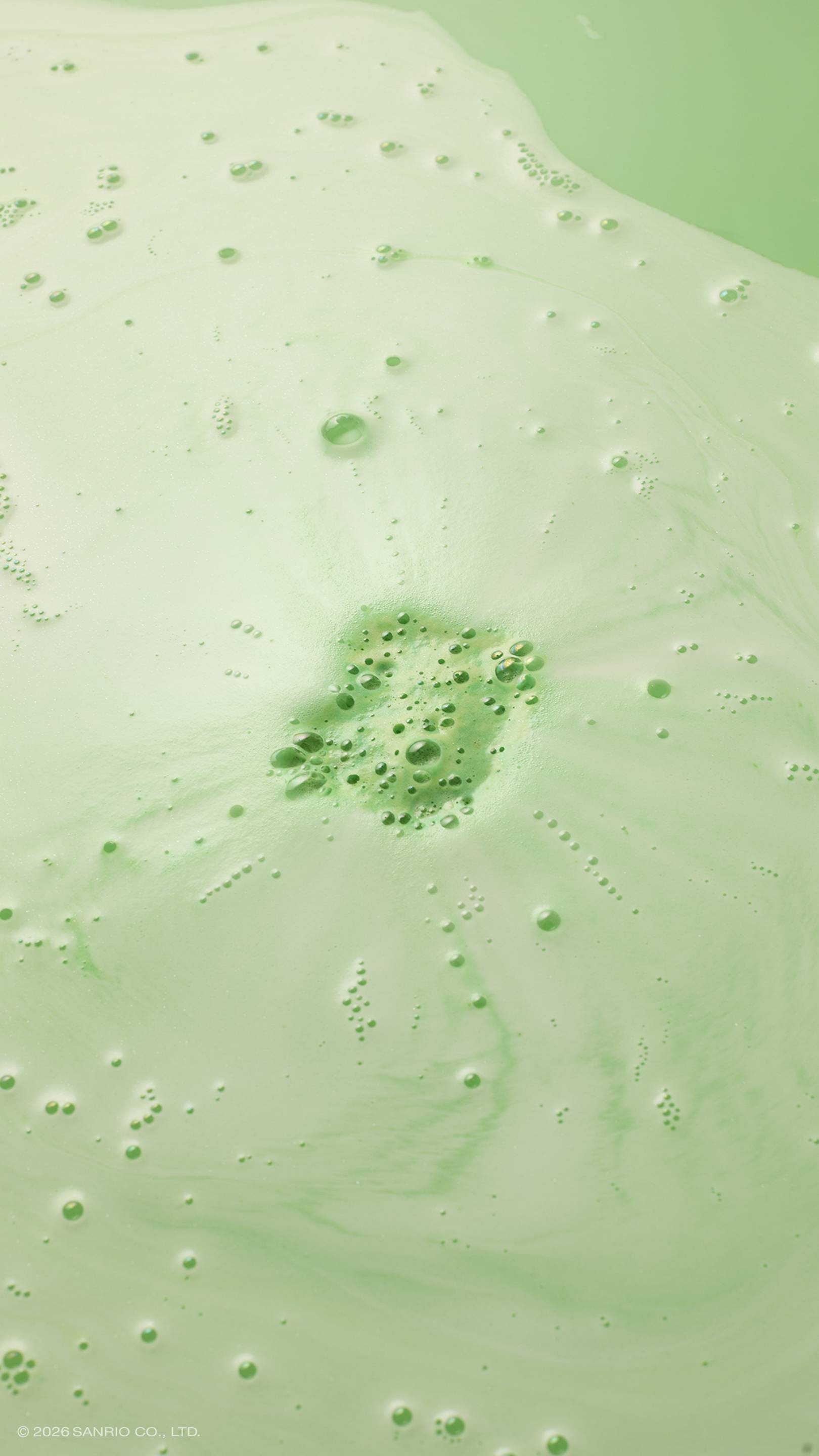 An aerial shot of lime-green bath water swirling with white foam and bubbles after using the "Kerokerokeroppi" bath bomb. In the centre, a cluster of vibrant green bubbles marks where a bath bomb has dissolved, with pale green and white ripples.