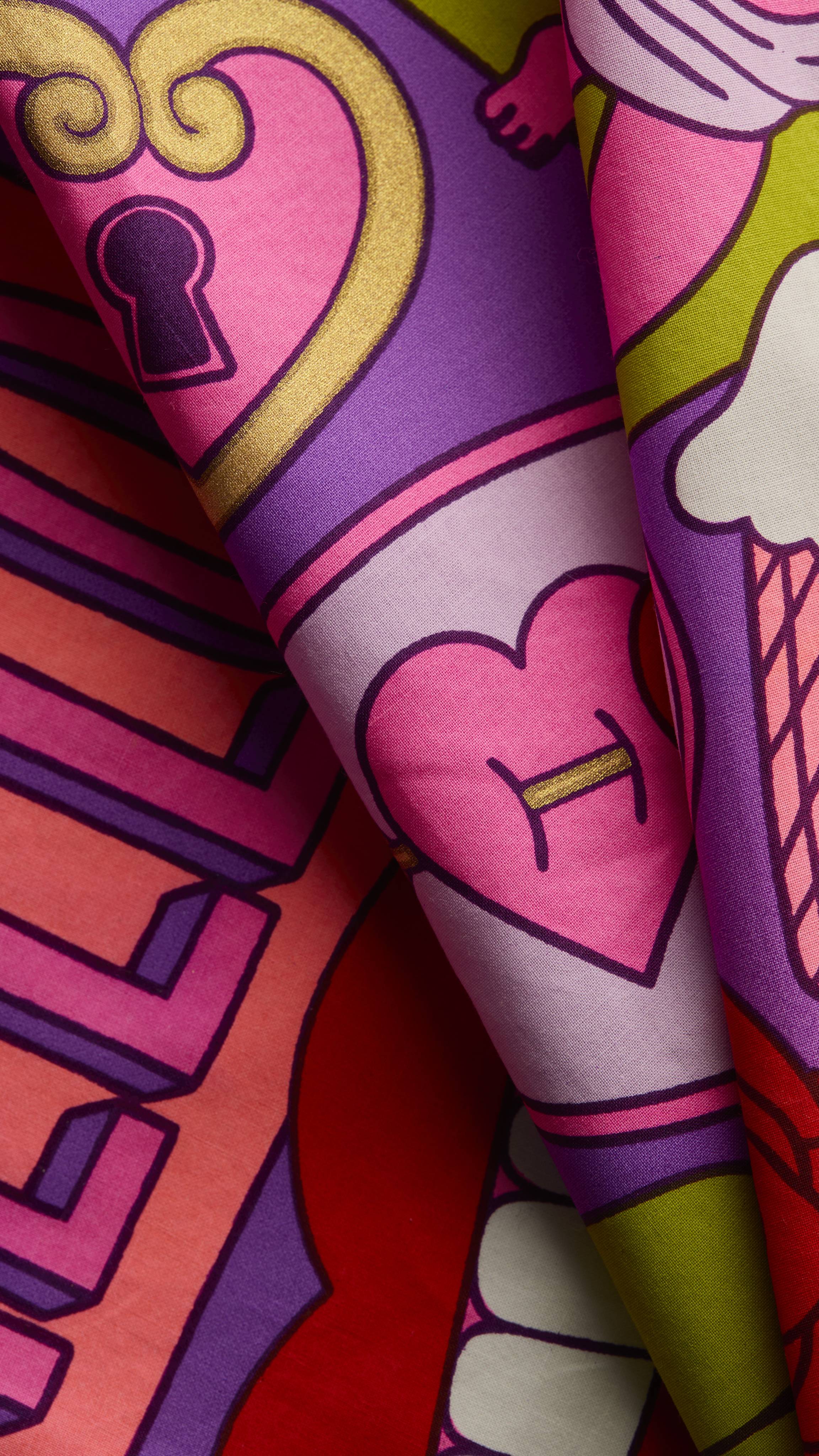 A close-up view of the Squeeze Knot Wrap fabric reveals a vibrant pattern on a purple background, featuring a pink and gold heart-shaped padlock and a pink heart illustration.