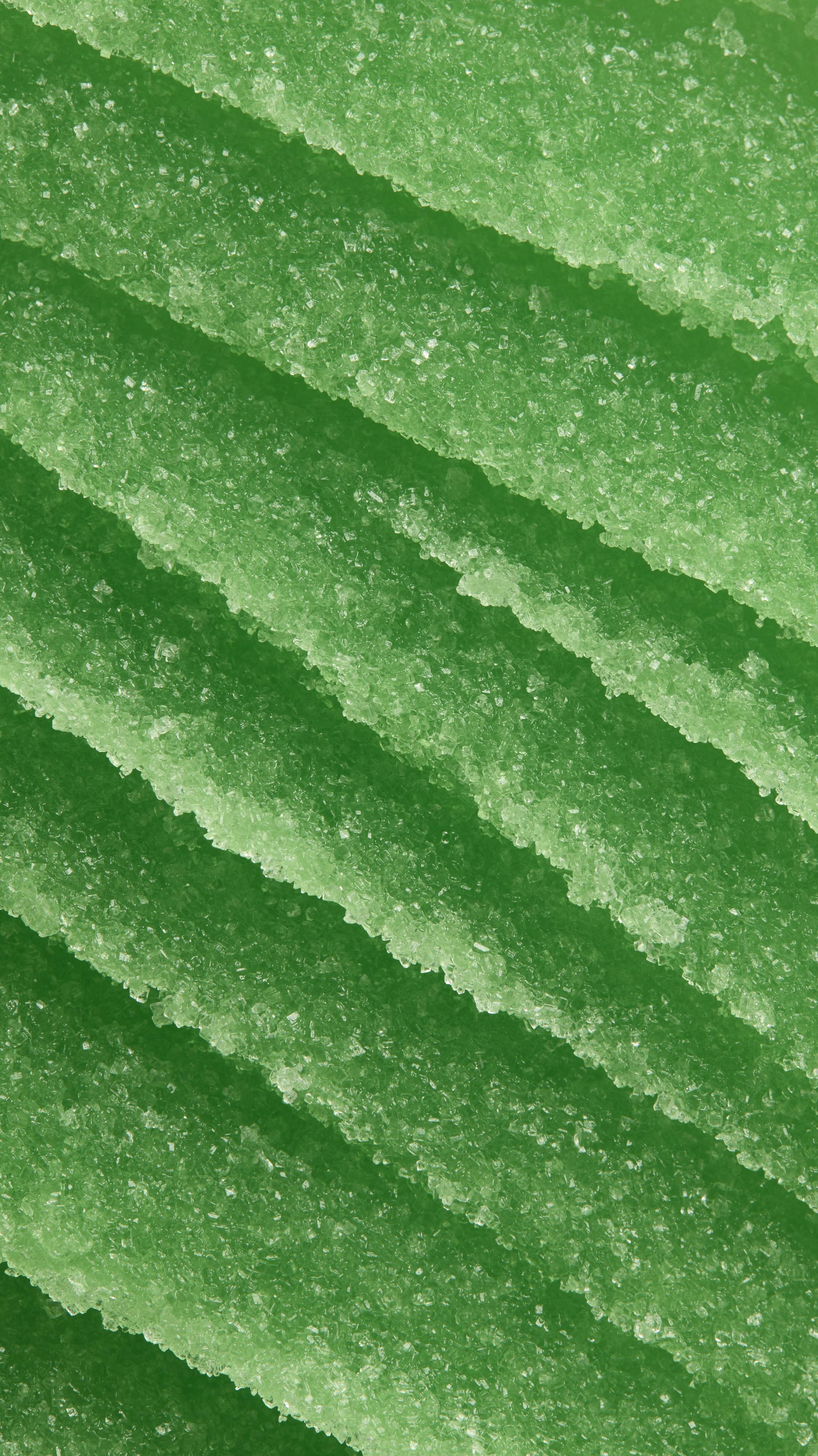 A close-up image showing the thick, grainy texture of Lush "French Kiss" lip scrub. The vibrant green scrub is spread in diagonal, overlapping ridges, highlighting its sugary consistency.