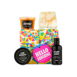 Hello Sunshine. A square gift box wrapped in colourful paper showing pink, blue and yellow suns and tied in a blue string with a pink product tag. There are four LUSH products placed around, including a soap, shower gel, body butter and body scrub. 