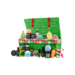 An open green wicker hamper with red straps overflows with festive Lush products, including bath bombs, shower gels and body lotions, with some shaped as Christmas favourites.