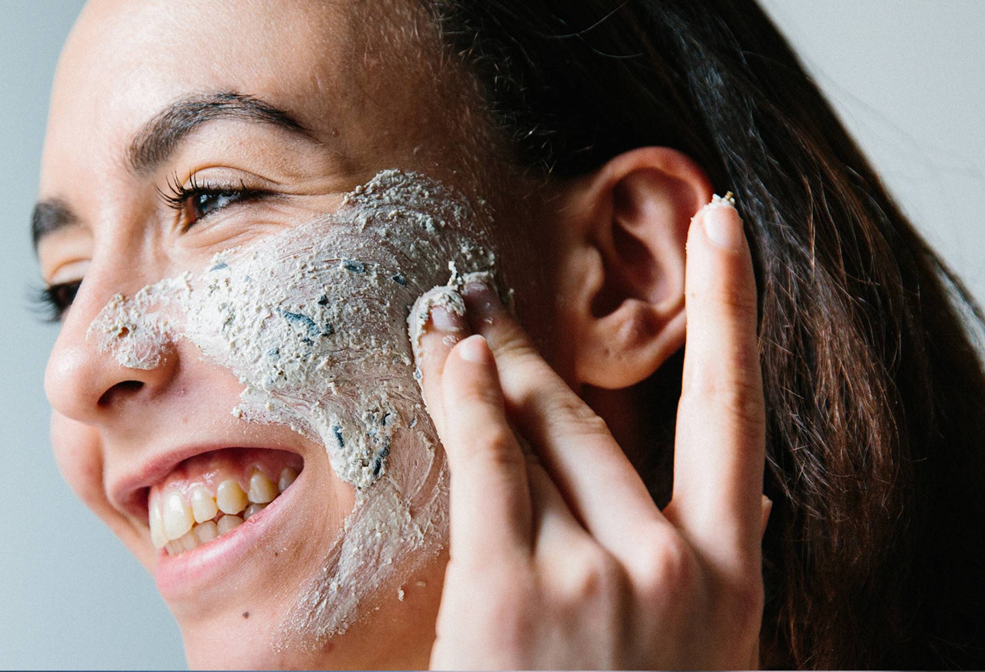A smiling face rubs thick, seaweed-packed, cream coloured BB Seaweed face mask into their outer cheek.