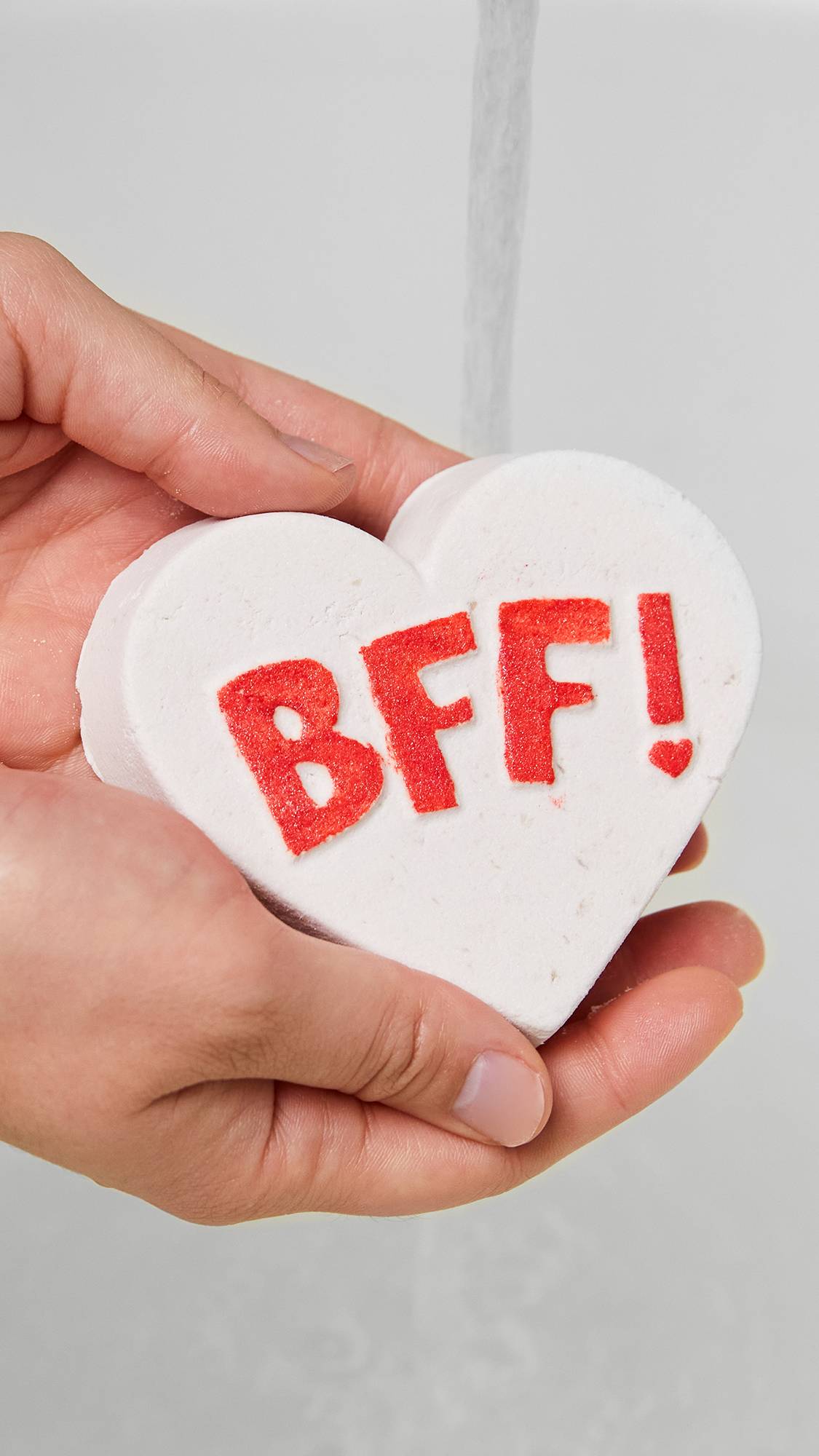 A close-up image of the model's hands gently holding the large white heart BFF bubble bar. 