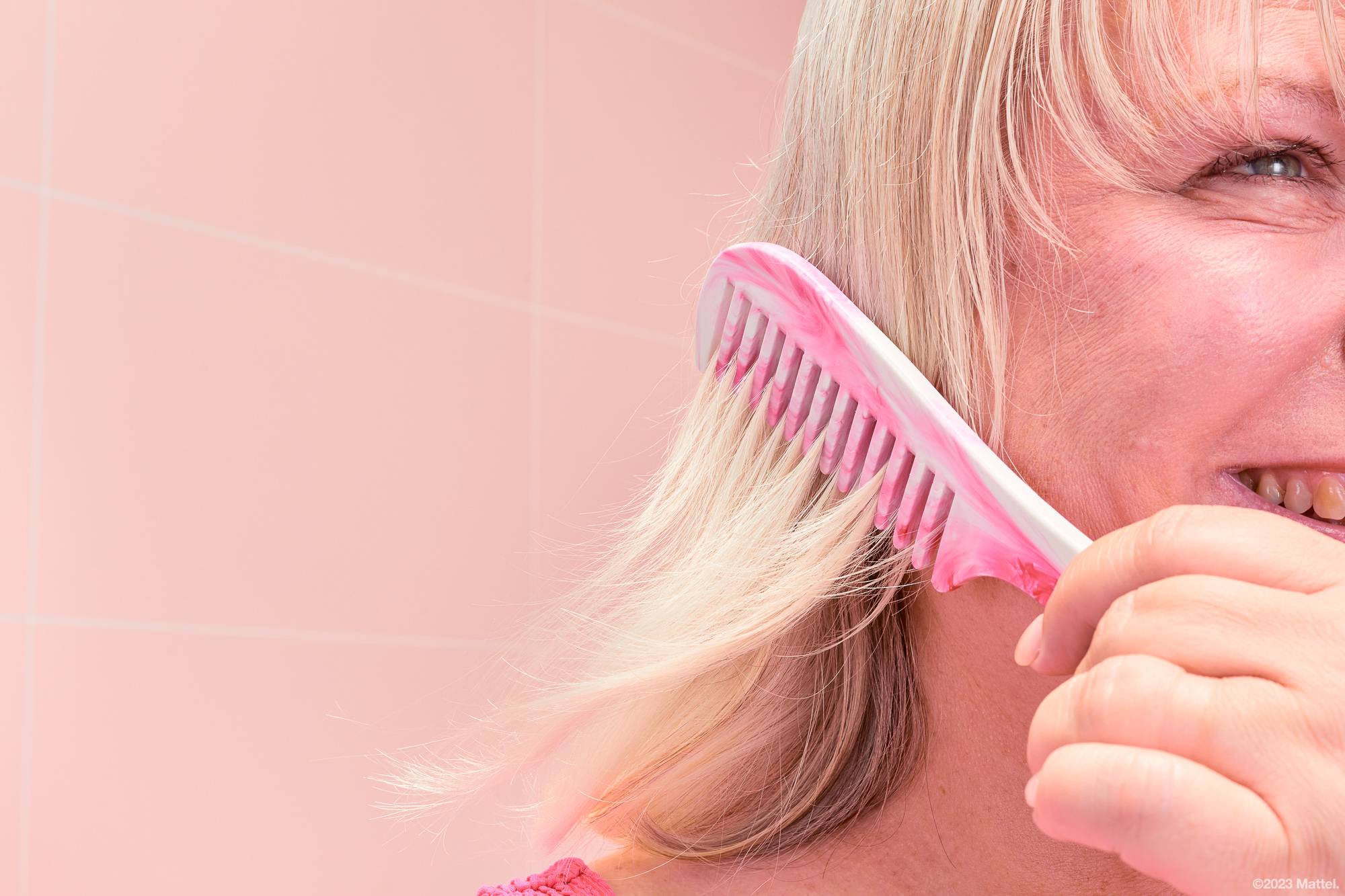 Image shows a close-up of the side of the model's face as they brush their hair with the pink and white marbled Barbie comb. 