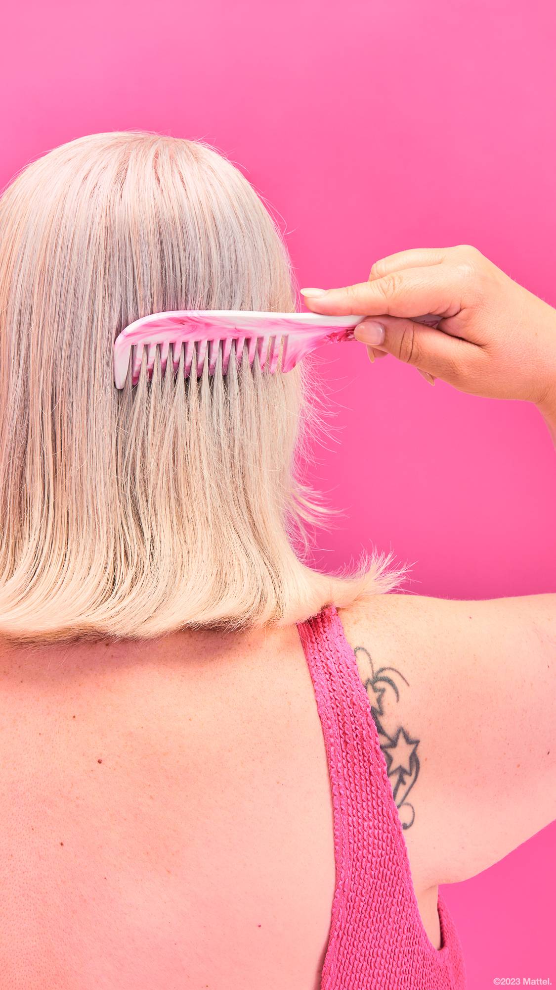Image shows the back of the model's head being brushed with the Barbie comb in front of a bright pink background.
