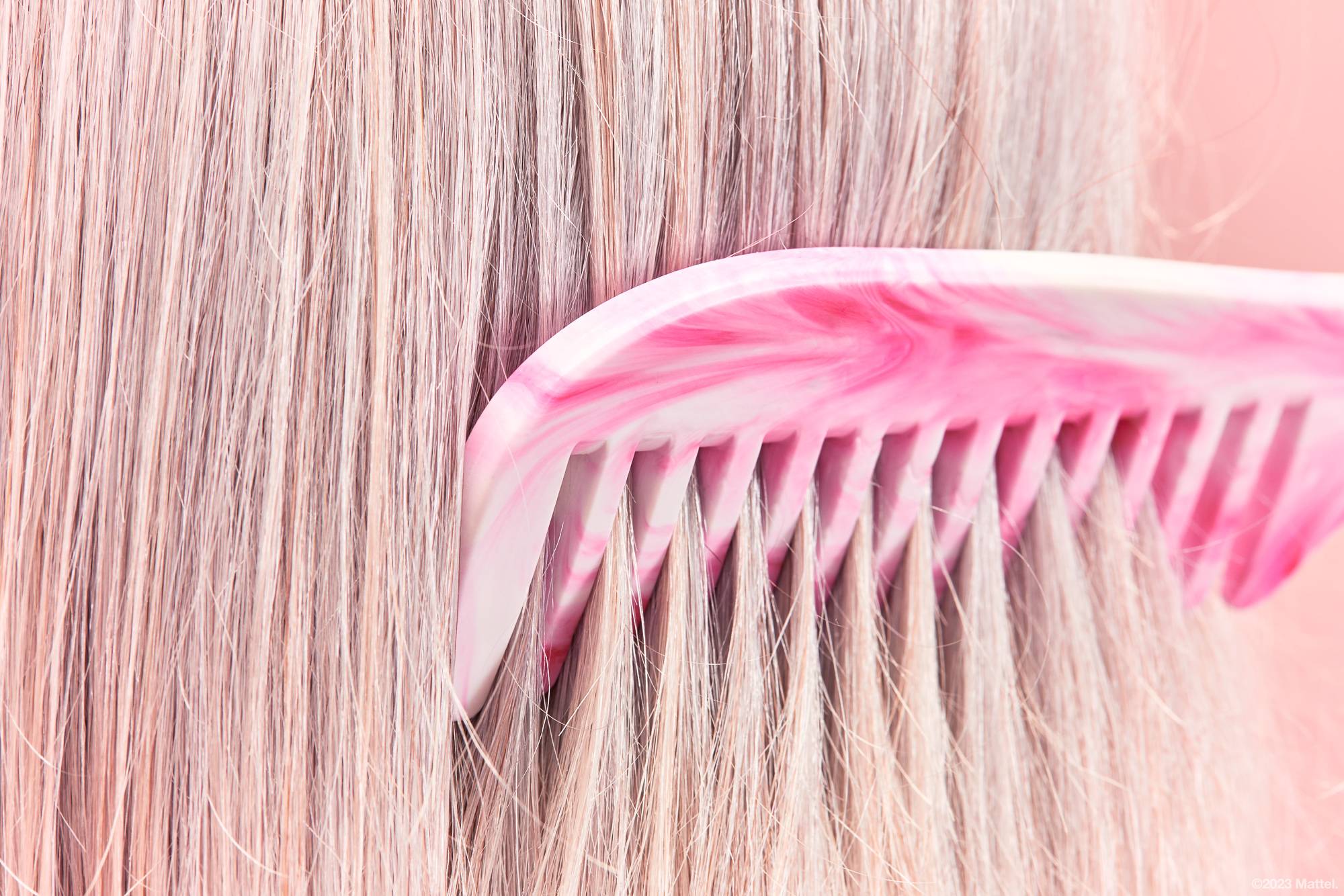 Image shows a super close-up of the marbled pink and white comb being brushed through straight blonde hair. 