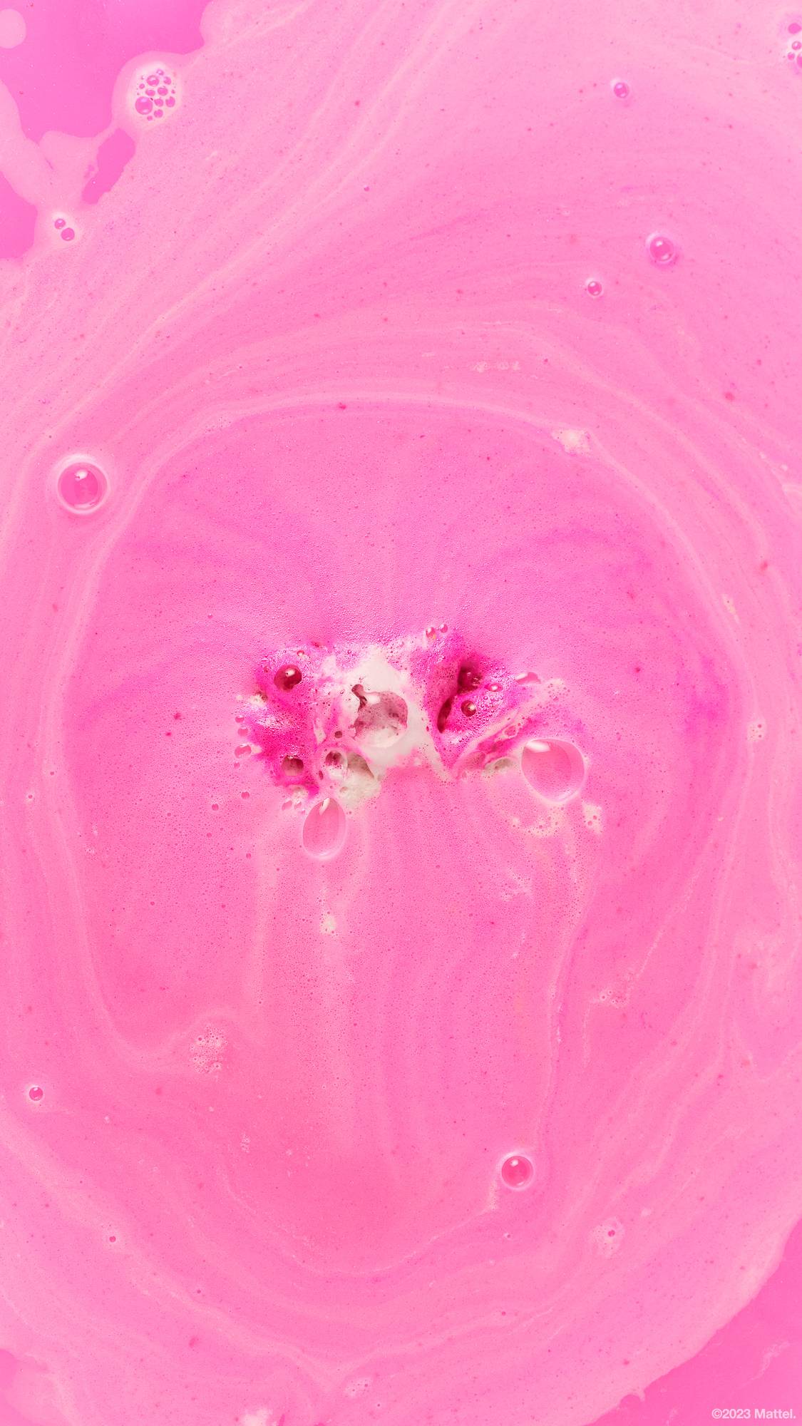 Barbie bath bomb almost completely diminished, floats on a foamy pink sea.