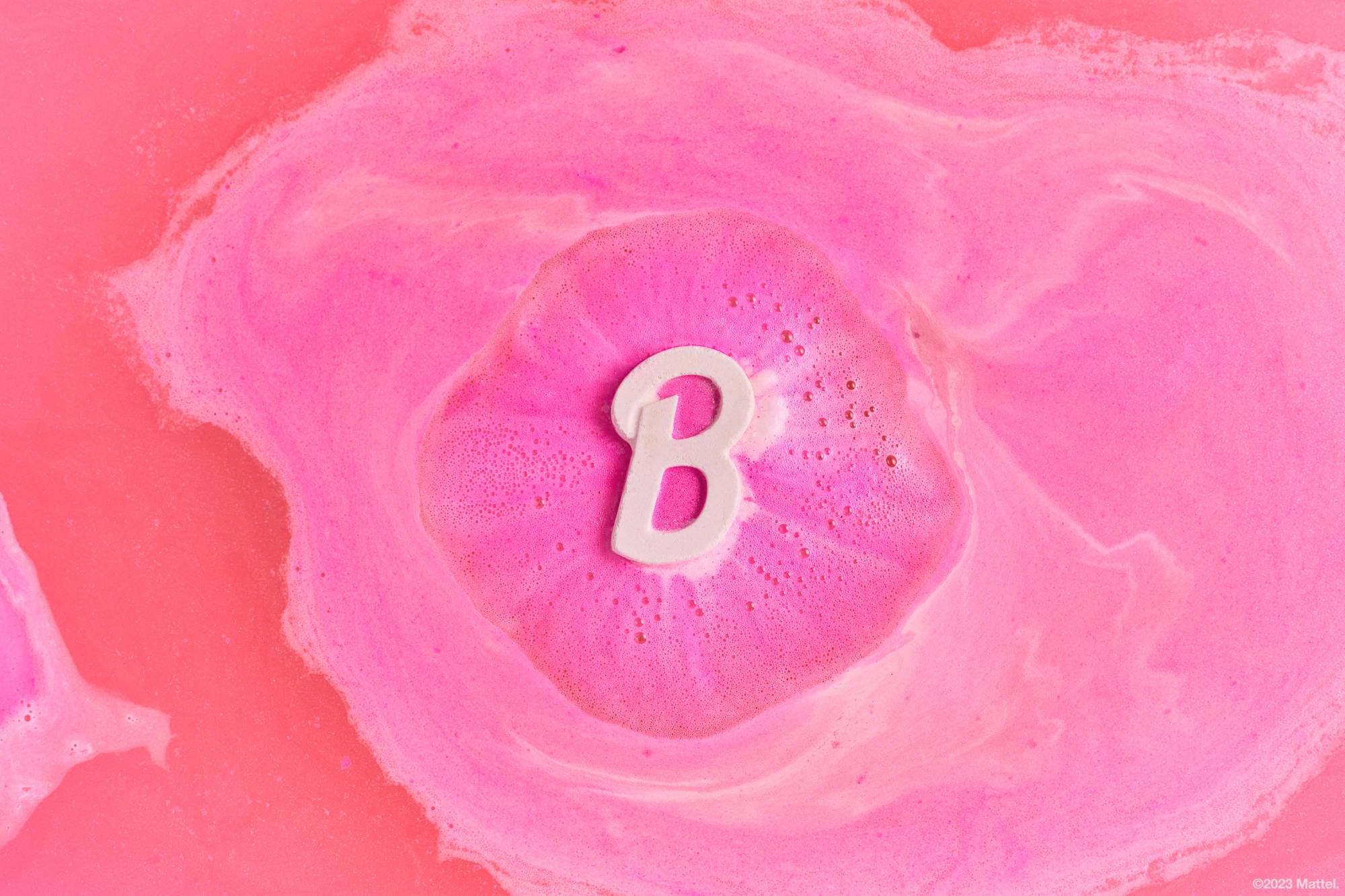 Barbie bath bomb floats gently on bathwater, slowly melting away to leave swirls of pink hues. 