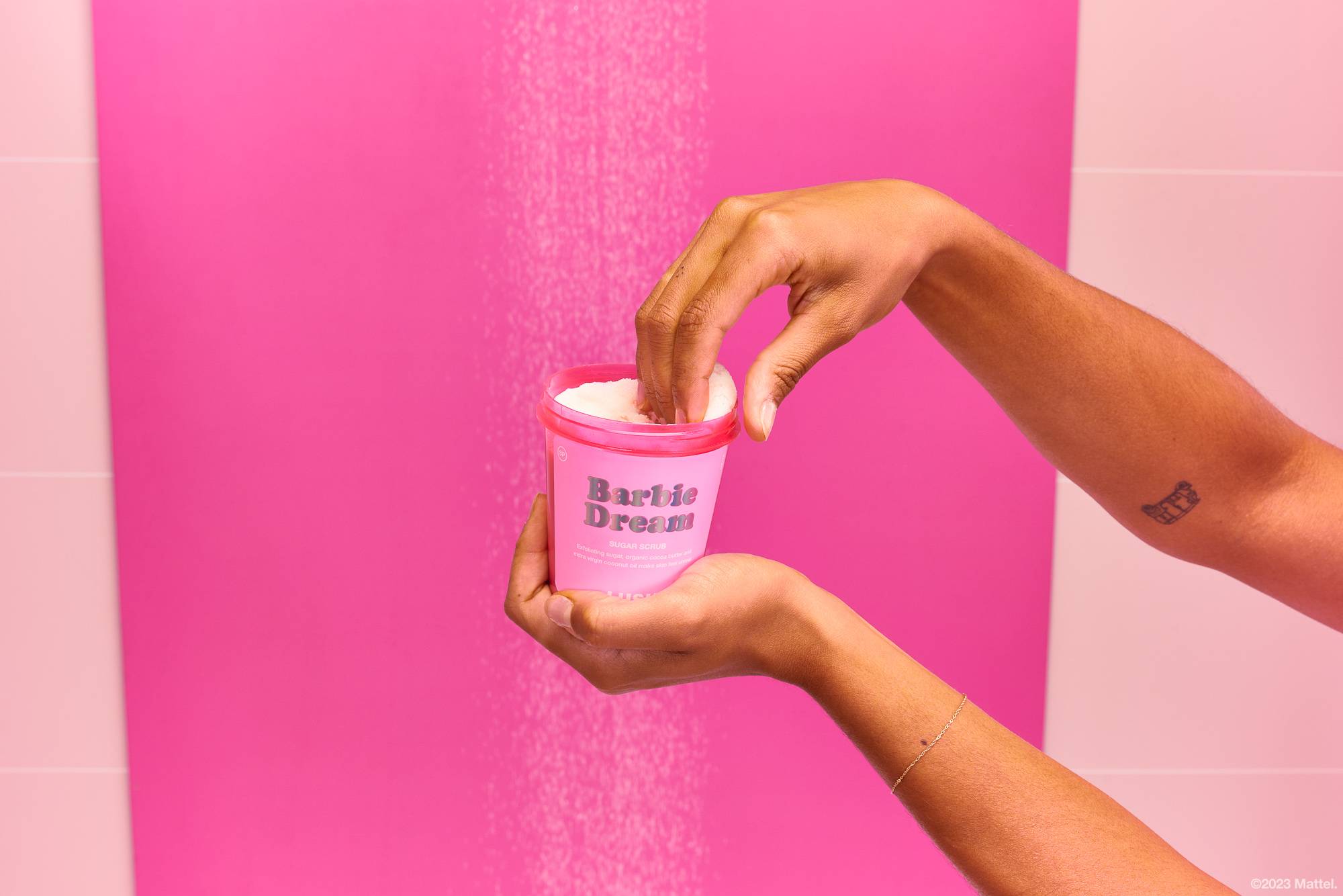 Model is in a pink shower, scooping out the Barbie Dream product from a pink LUSH "bring it back" pot as the water runs behind.
