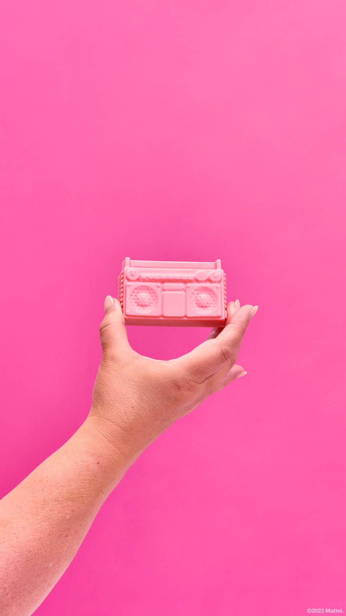 Image shows a close-up of model's hand holding the pastel pink boombox-shaped soap on a hot pink background. 