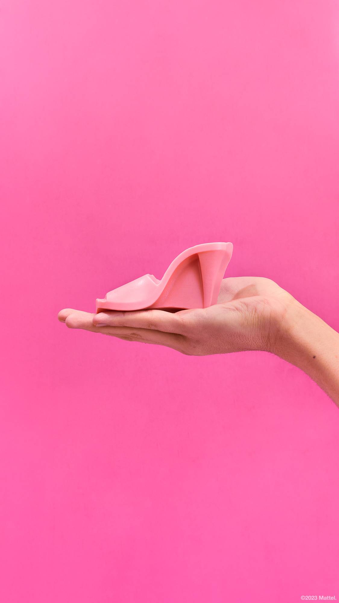 Image shows a close-up of the model's hand holding the perfect, pink, open-toed heel soap on a hot pink background. 
