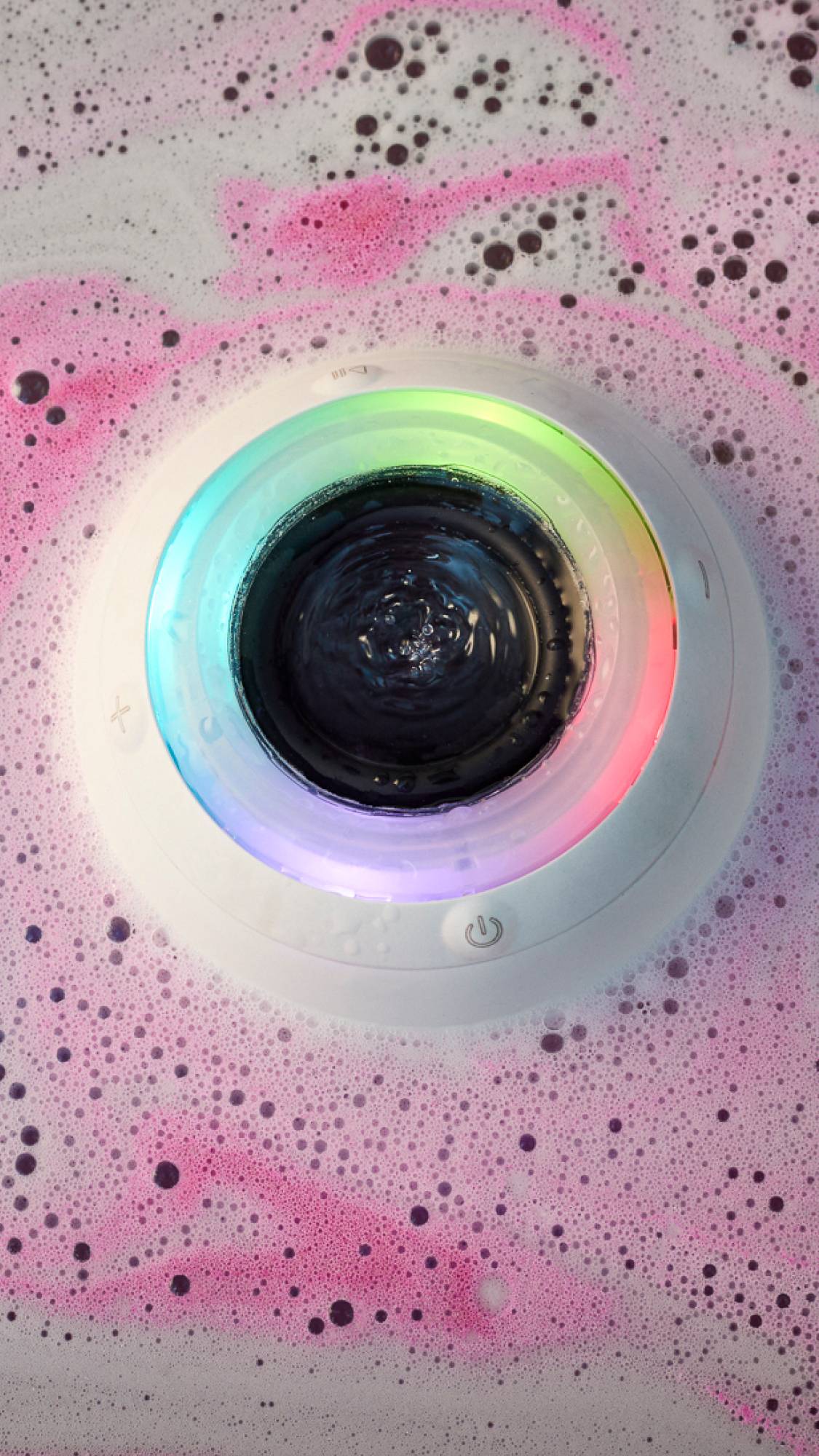 An aerial view of the Bath Bot in the tub surrounded by the swirls of a bath bomb. The illuminated ring at the top is glowing all the colours of the rainbow. 