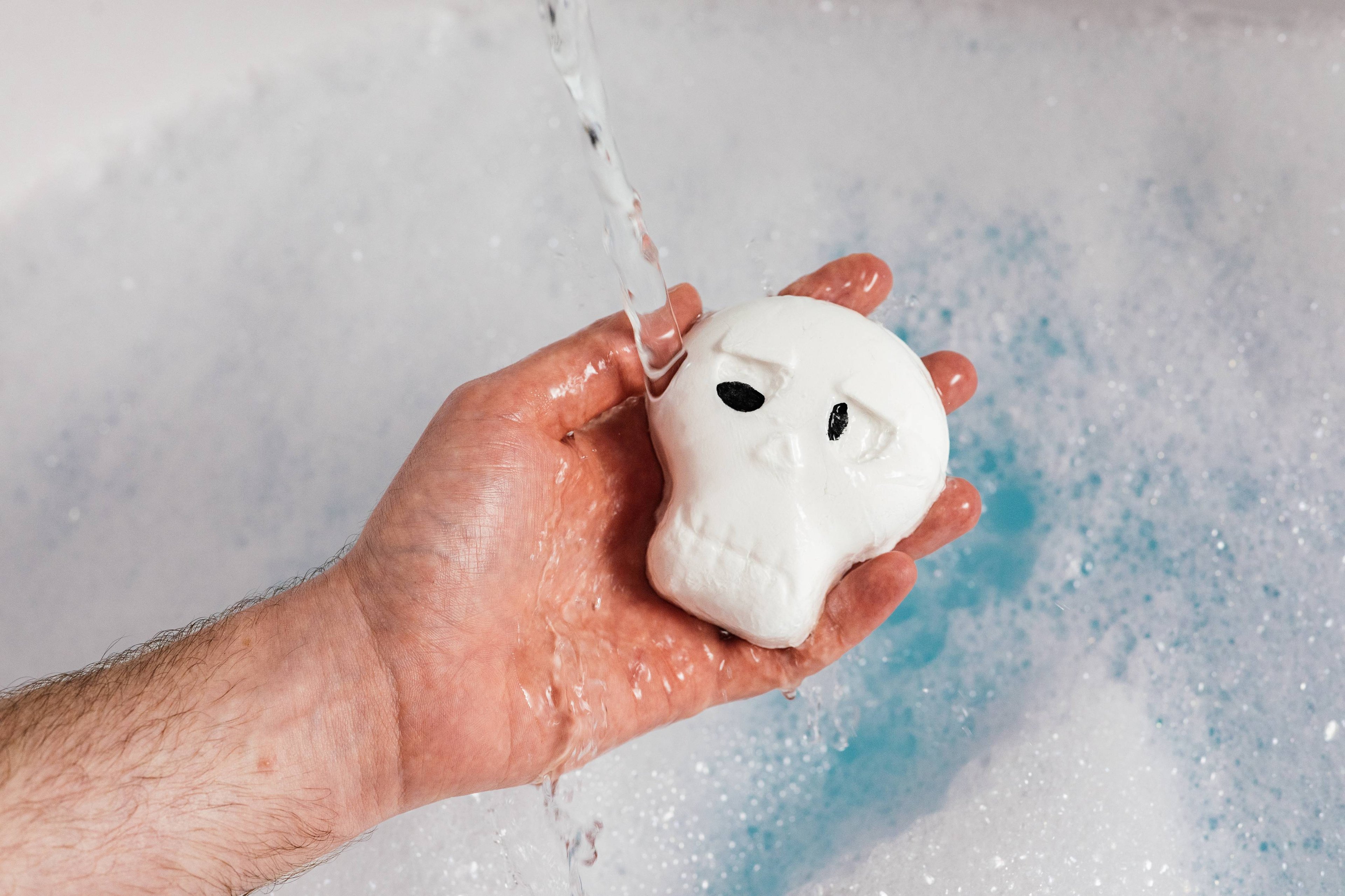 Image shows model holding the bubble bar under running water as it creates a thick blanket of foamy bubbles.