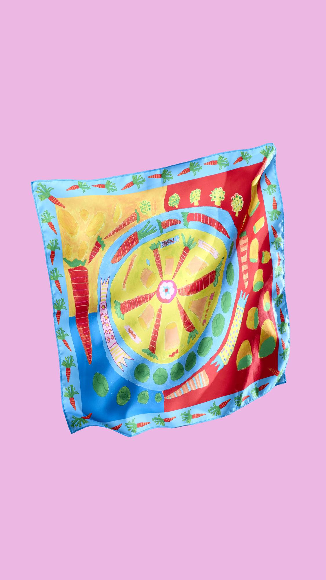 A square, colorful Lush "Veggie Christmas Dinner" Knot Wrap with a festive, food-themed pattern. The design includes carrots, peas, and sprouts in a variety of colors, including red, blue, green, and yellow.