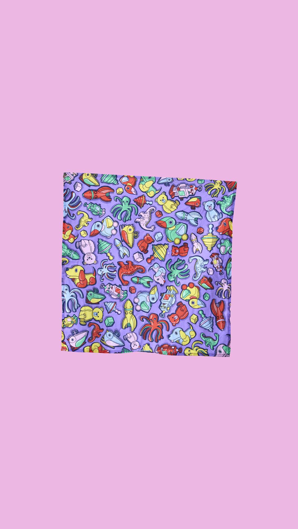 A vibrant, reusable Lush "Vintage Toys" Knot Wrap. The square fabric has a purple background with a colorful, repeating pattern of old-fashioned toys like wooden animals, rubber ducks, rockets, and teddy bears.