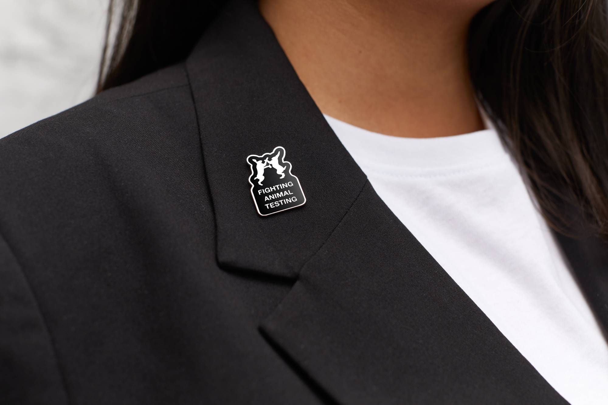 Image is a close-up of the model wearing a black blazer with the Fighting Animal Testing pin badge secured to the lapel.