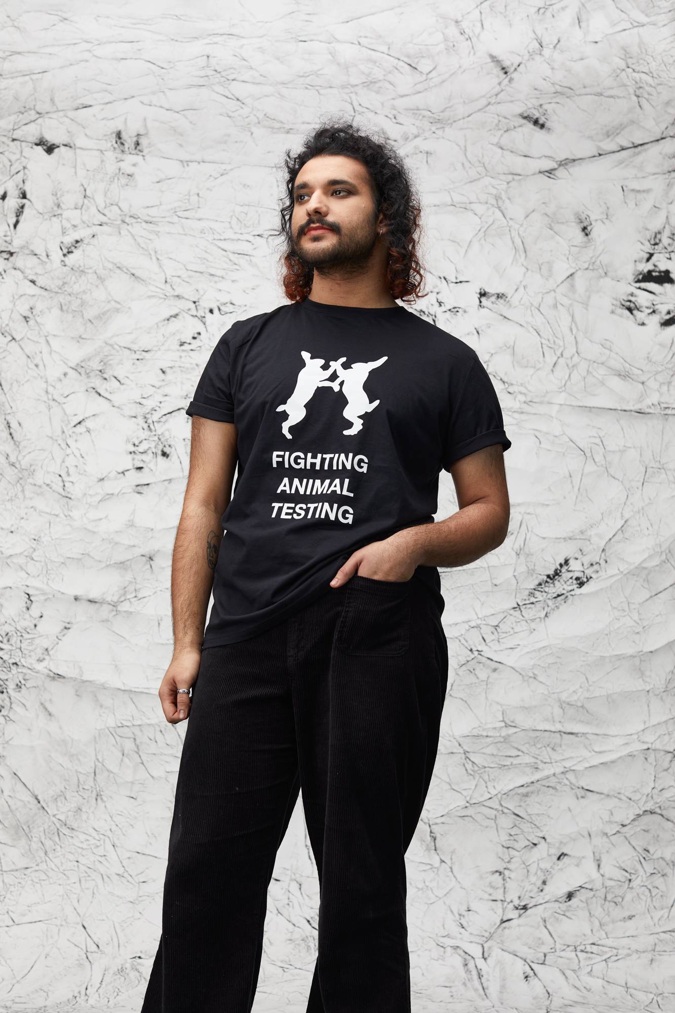 Model stands in front of marbled background wearing the t-shirt with black trousers.