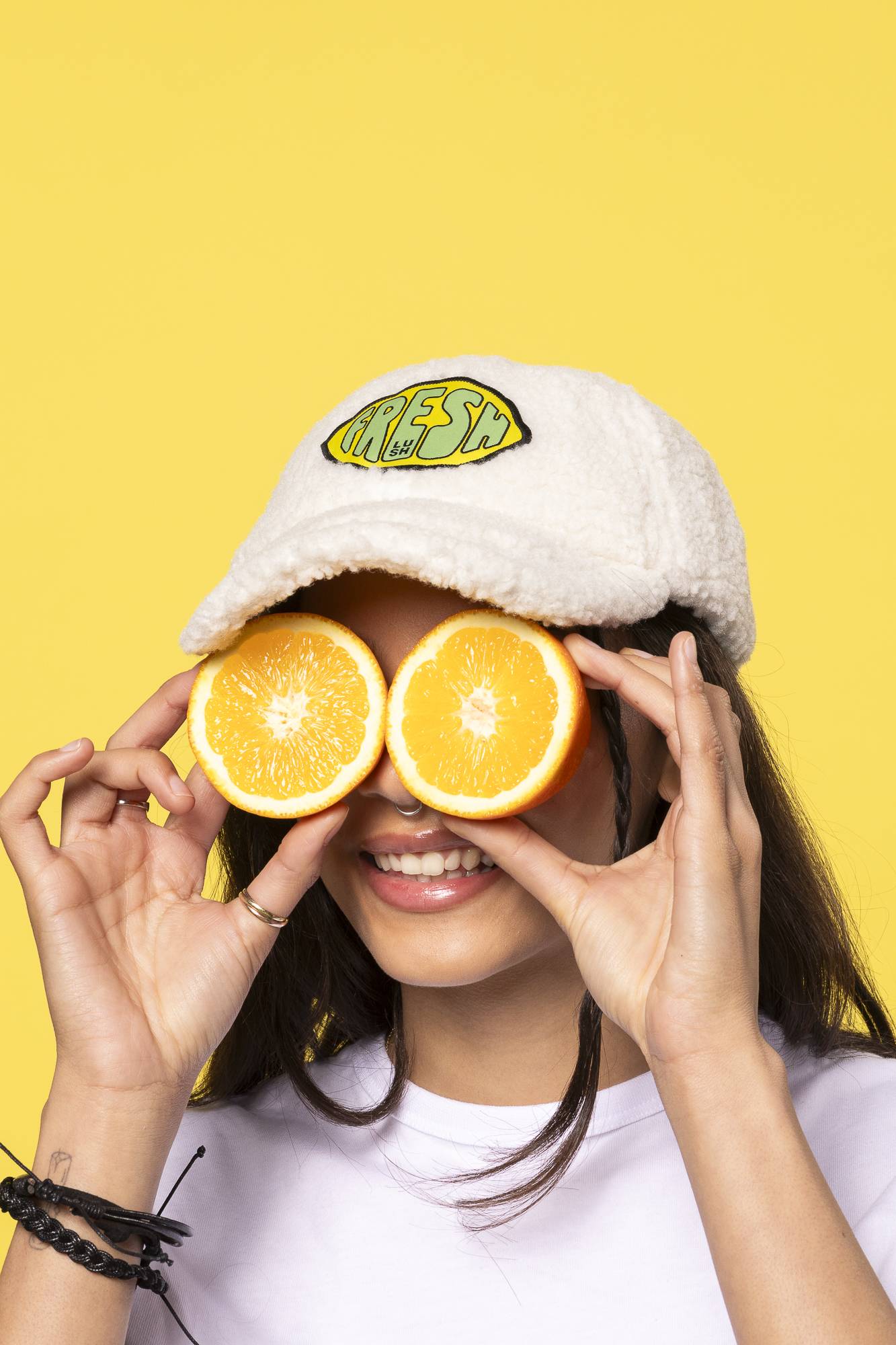 Image shows the model wearing the Fresh Values Iron-on patch on their cap hat as they hold orange slices to their eyes. 