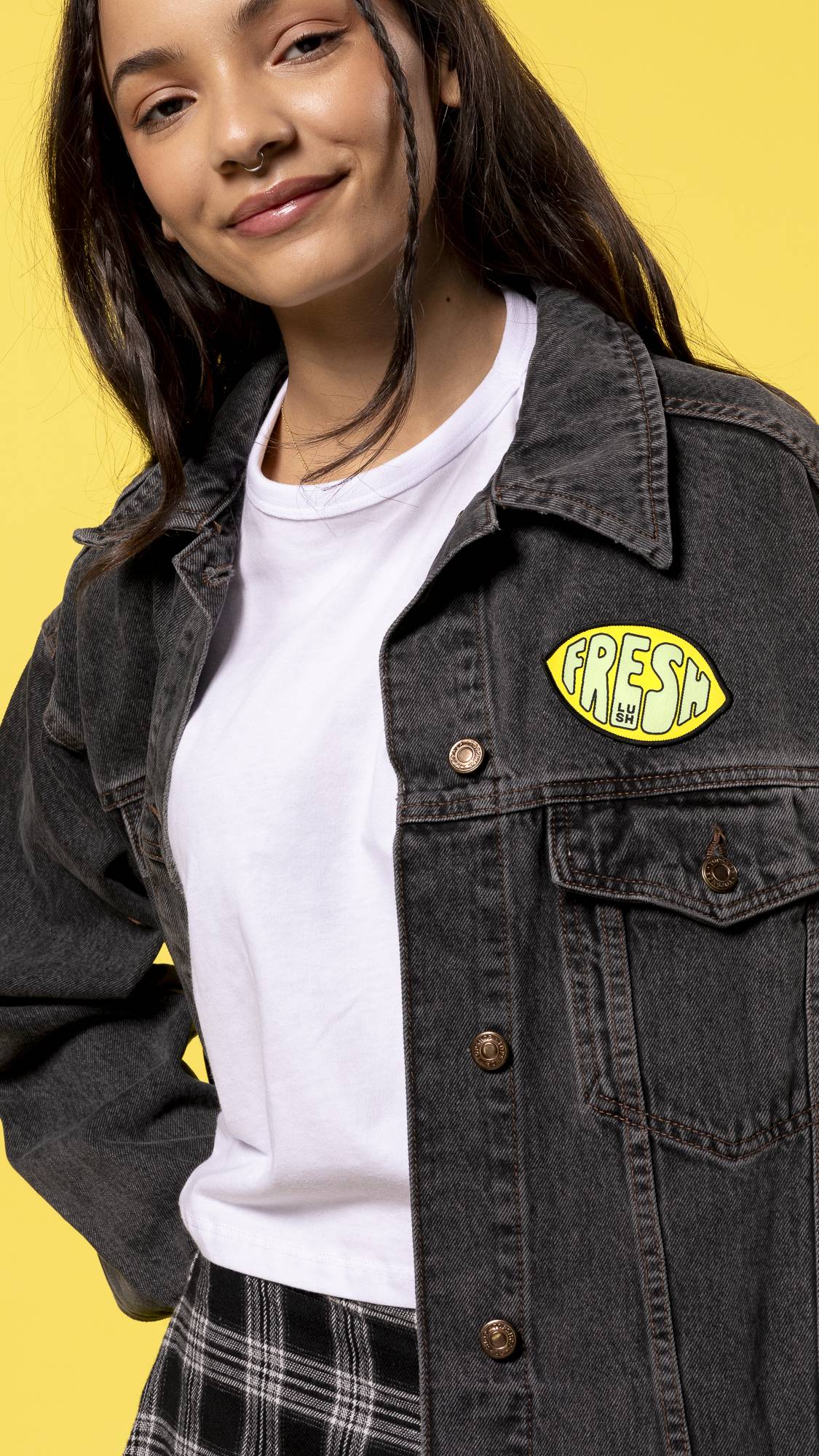 Model is stood on a bright yellow background in a dark denim jacket with the iron-on patch above the breast pocket. 