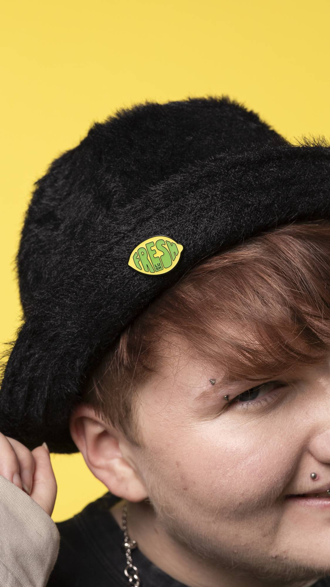 A close-up of the Fresh Values pin badge on a black, fuzzy hat. On a bright yellow background.