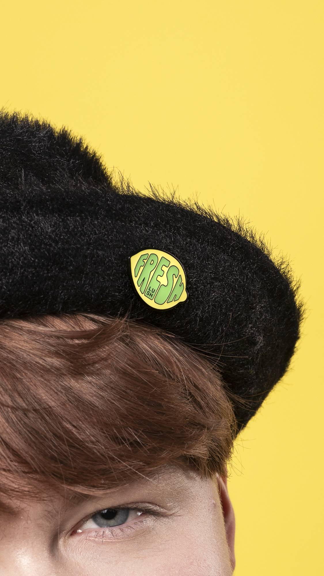A super close-up of the model's face and head wearing a black hat with the Fresh Values pin badge attached.