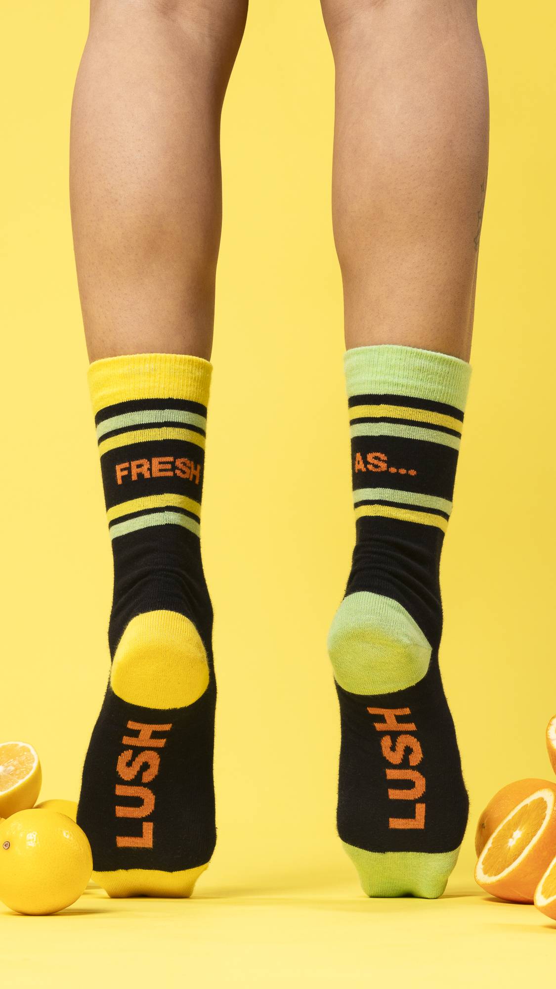 A shot of the model's calves down shows them standing on tip toes showing the Fresh Values socks, surrounded by citrus fruits. 