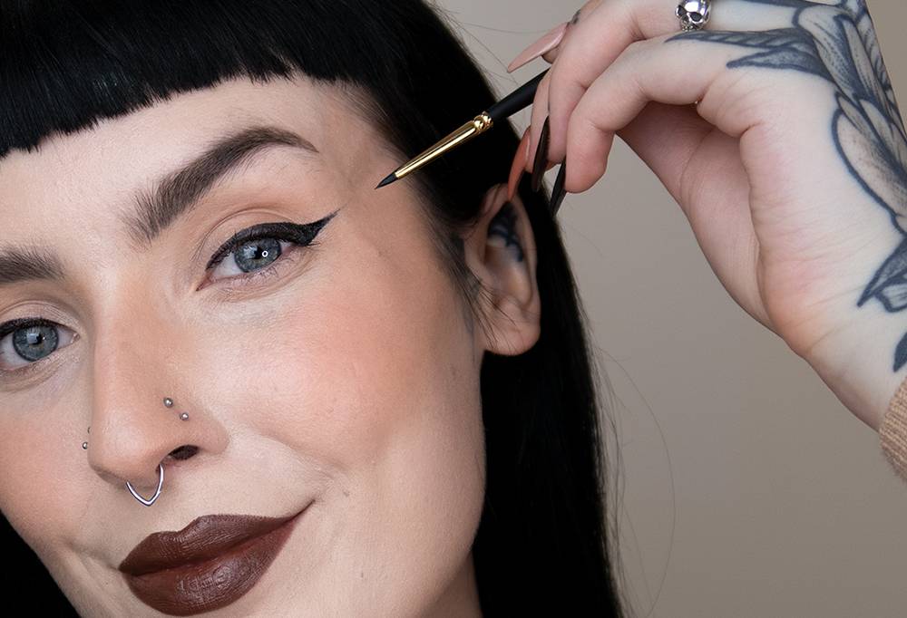 A person smiles, having created a perfect 'cat eye', using black eyeliner and a tiny, pointed liner brush - Get In There.