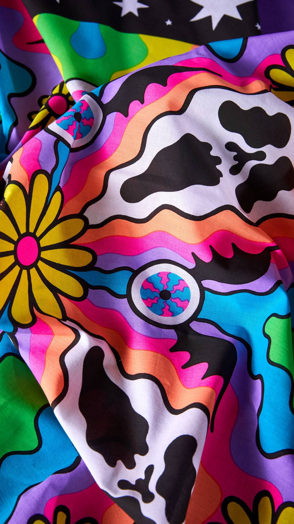 The image shows a close-up of the 'Cosmic Gathering' knot wrap. The vibrant, multi-coloured fabric is folded, showcasing a psychedelic pattern with flowers, wavy stripes, and stars.